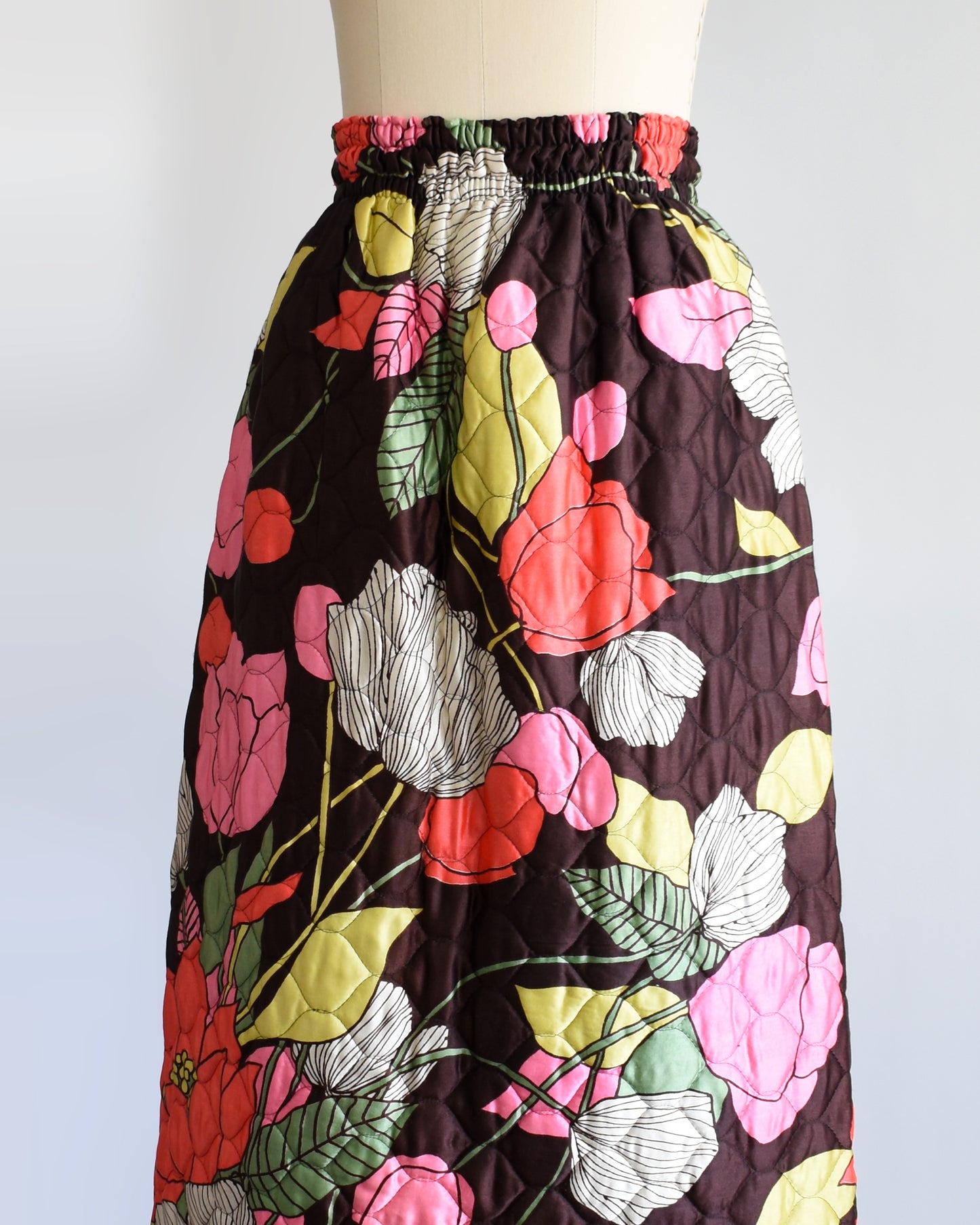 side front view of a vintage 1970s quilted skit that has a colorful floral print on a mannequin against a white background