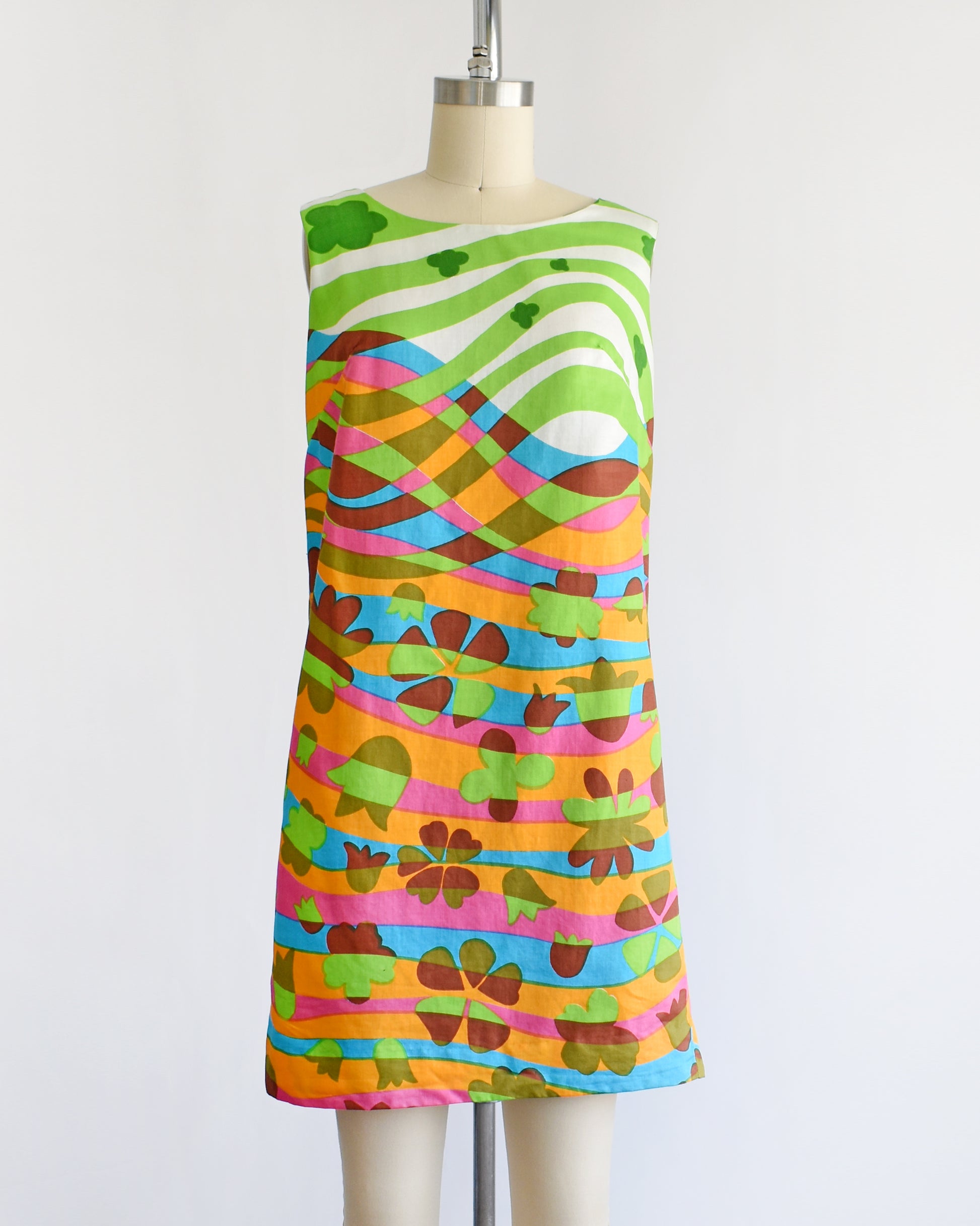 A vintage 1960s sleeveless dress displayed on a cream mannequin against a plain white background. The dress features a vibrant, multicolored abstract pattern with wavy horizontal bands in green, pink, orange, blue, yellow, and brown.