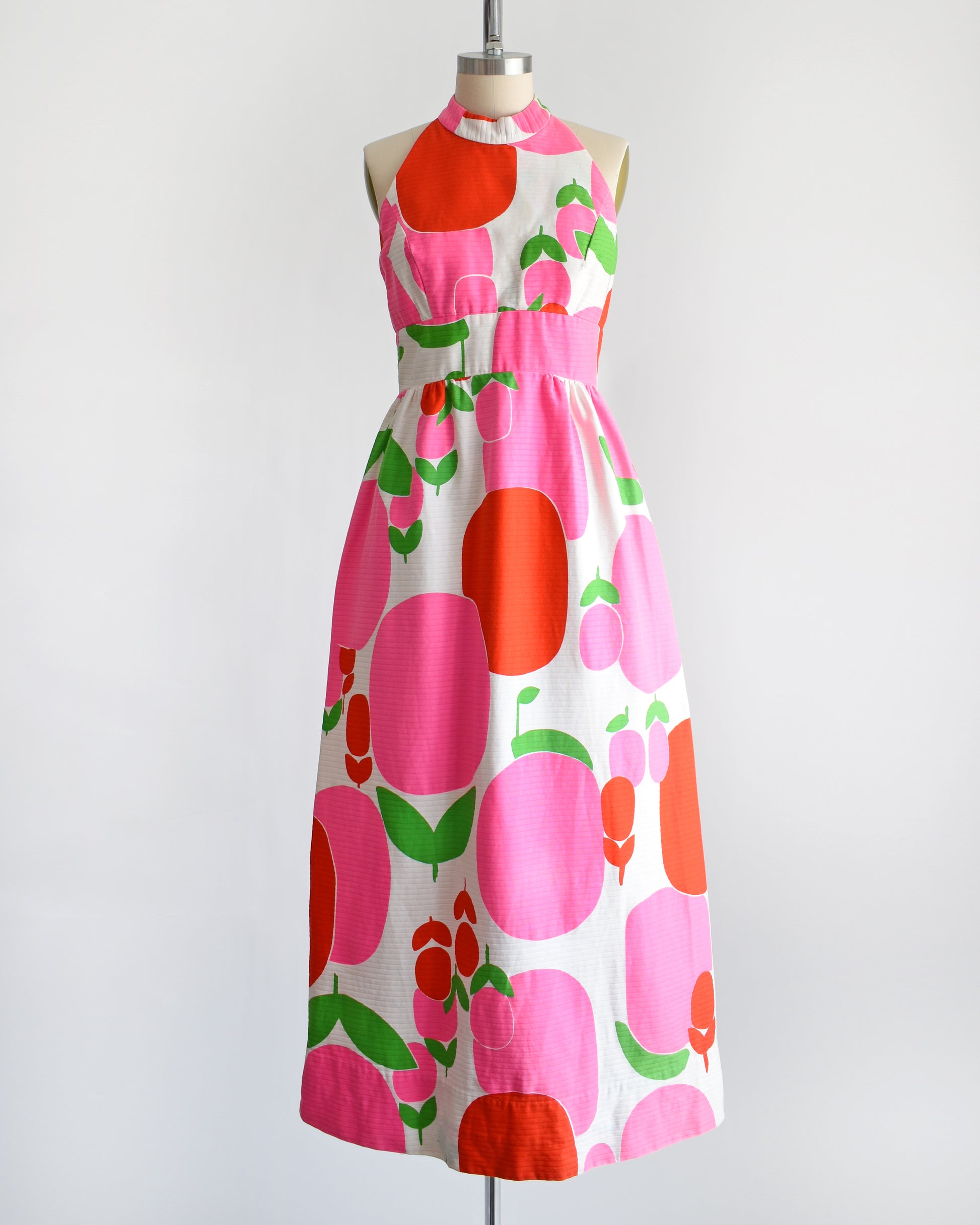 a vintage 1970s maxi dress by Malia that is white with a large red and pink fruit/floral print.