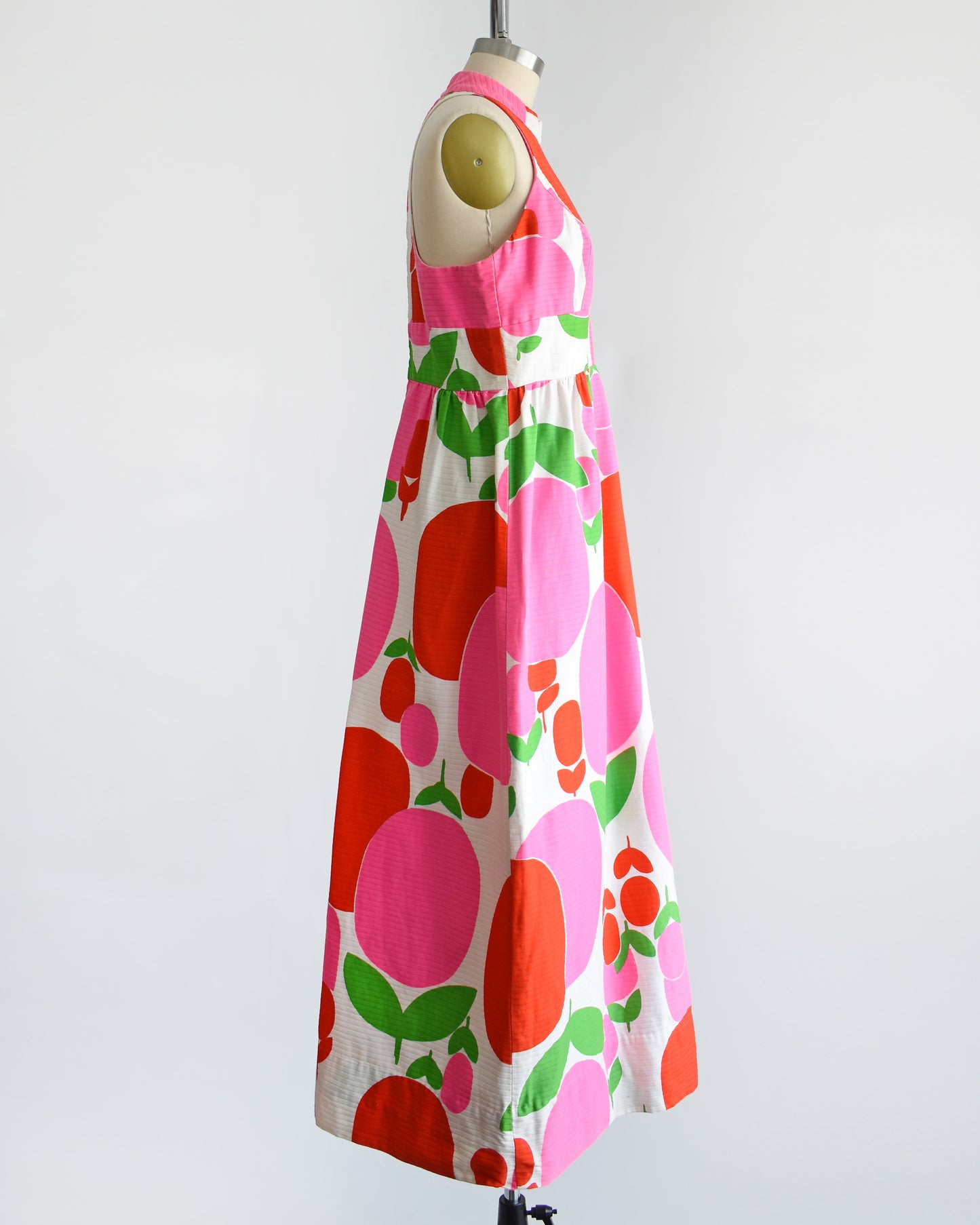 side view of a vintage 1970s maxi dress by Malia that is white with a large red and pink fruit/floral print.