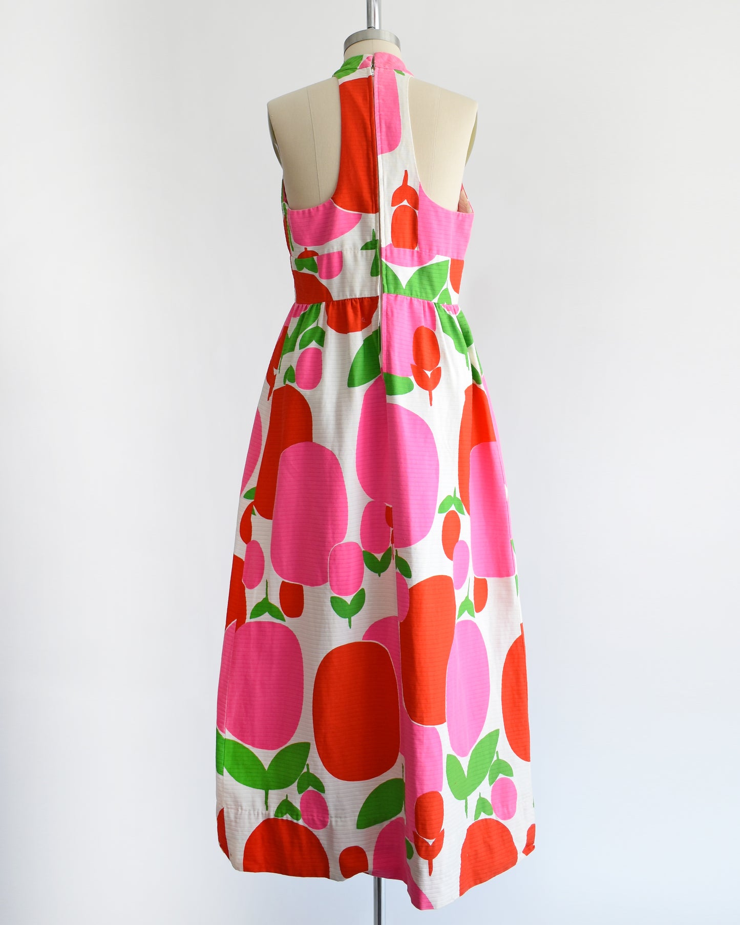 back view of a vintage 1970s maxi dress by Malia that is white with a large red and pink fruit/floral print.