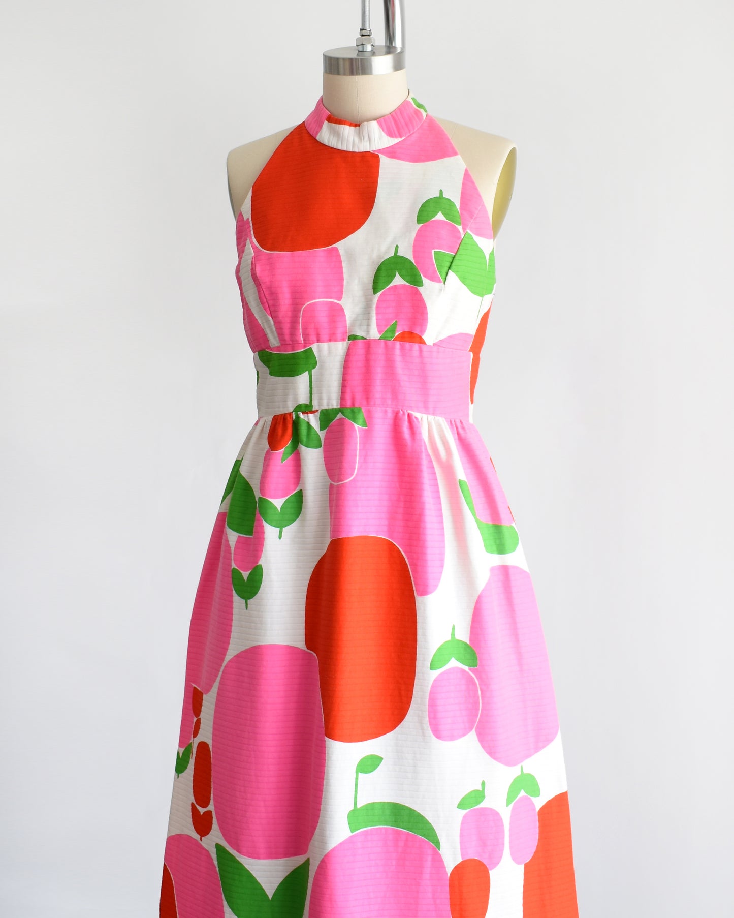 side front view of a vintage 1970s maxi dress by Malia that is white with a large red and pink fruit/floral print.