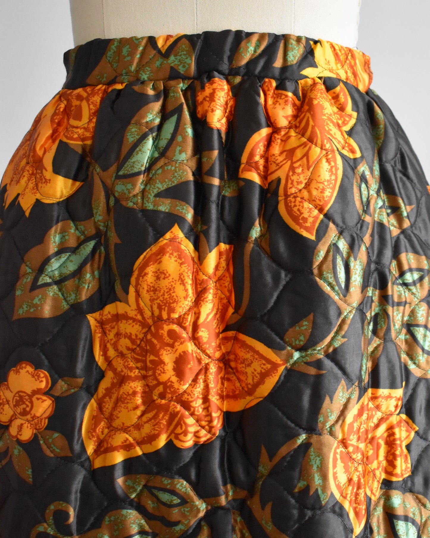 close up of the waist and hip area of a vintage 1970s dark brown and orange floral patterned maxi skirt on a mannequin against a white background