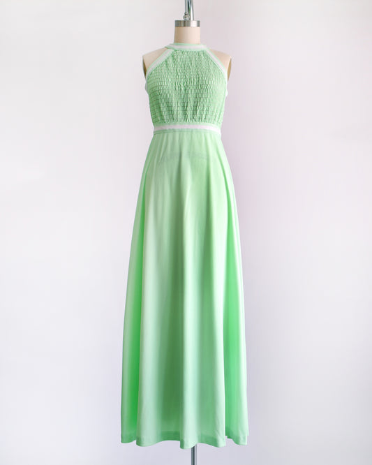 a vintage 1970s mint green sleeveless halter maxi dress with a smocked bodice and a flared skirt, displayed on a dress form against a plain light background.