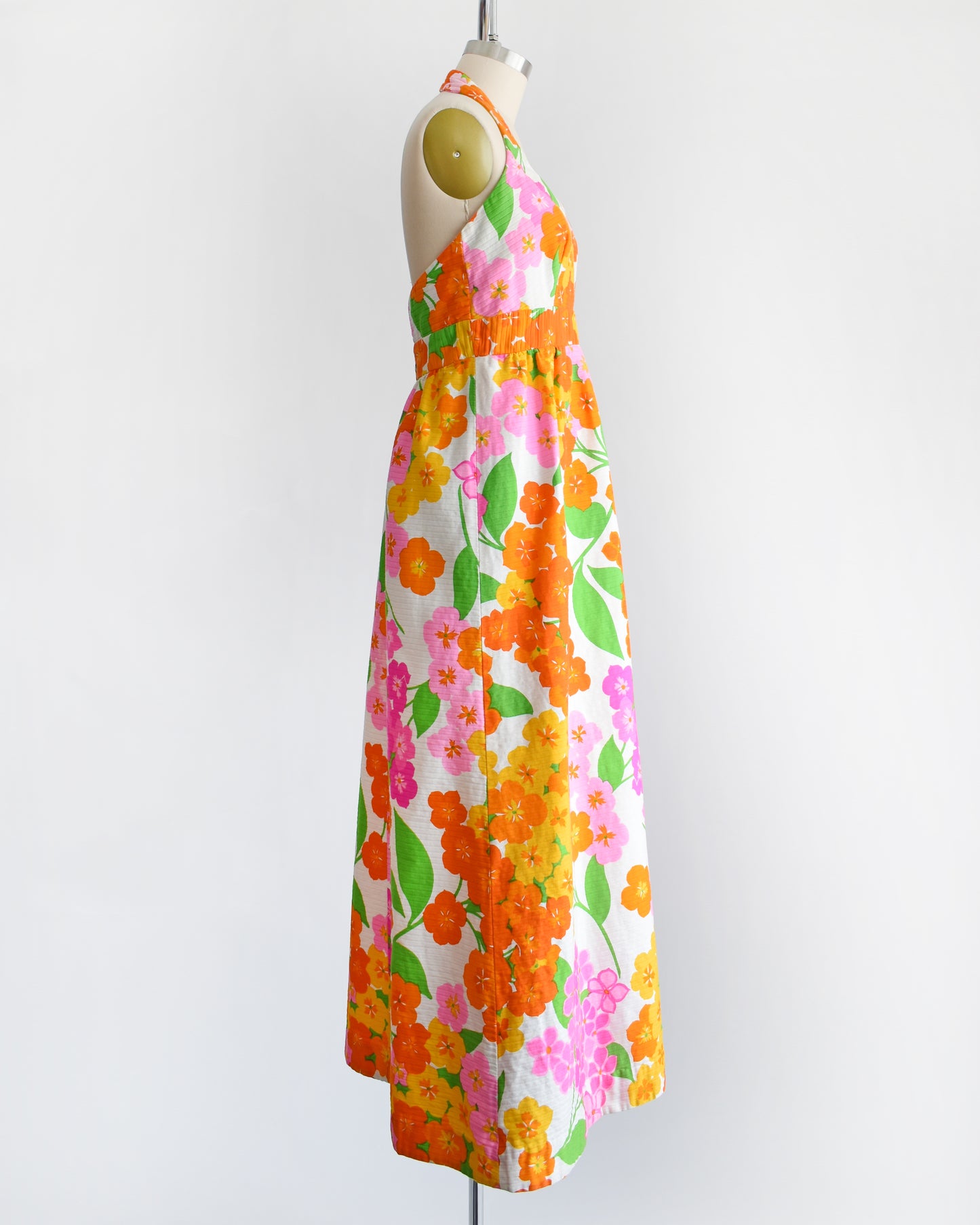 side view of a vintage 1970s Hawaiian floral maxi dress by Malia. The dress is made from white ribbed cotton and has a large pink, yellow, orange, and green floral print covering the dress.