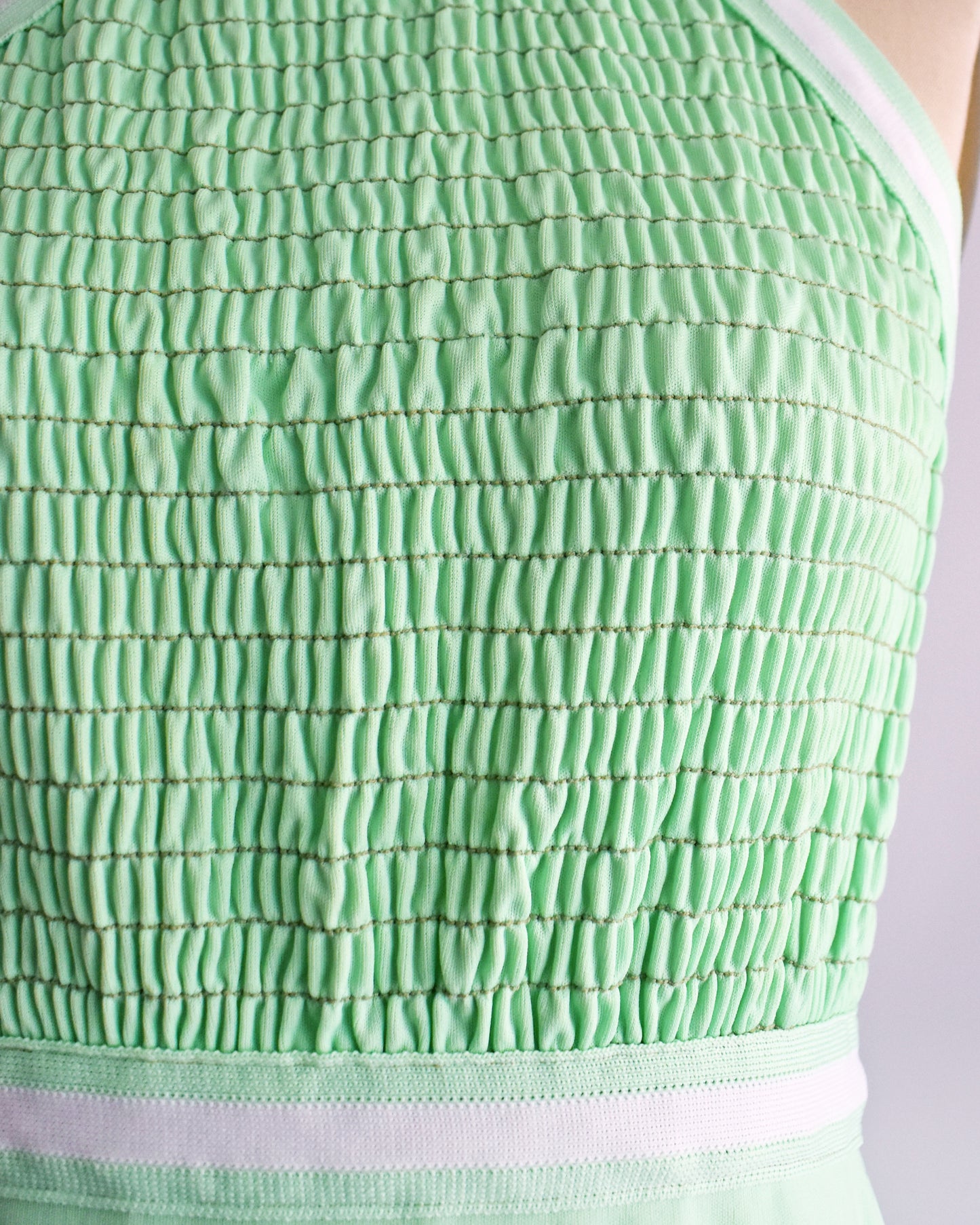 Close-up of a mint green smocked fabric garment, showing the textured grid stitching and a white horizontal trim band.