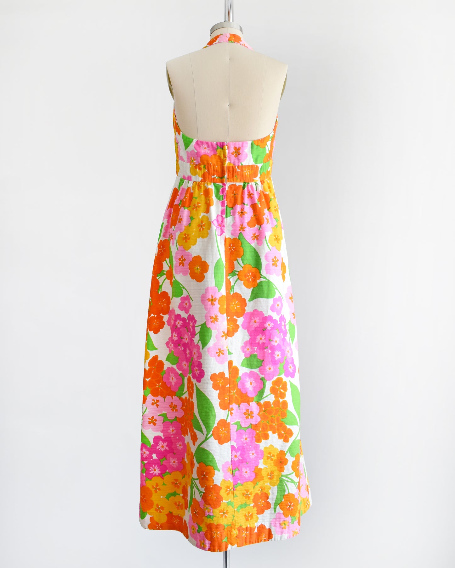 back view of a vintage 1970s Hawaiian floral maxi dress by Malia. The dress is made from white ribbed cotton and has a large pink, yellow, orange, and green floral print covering the dress.