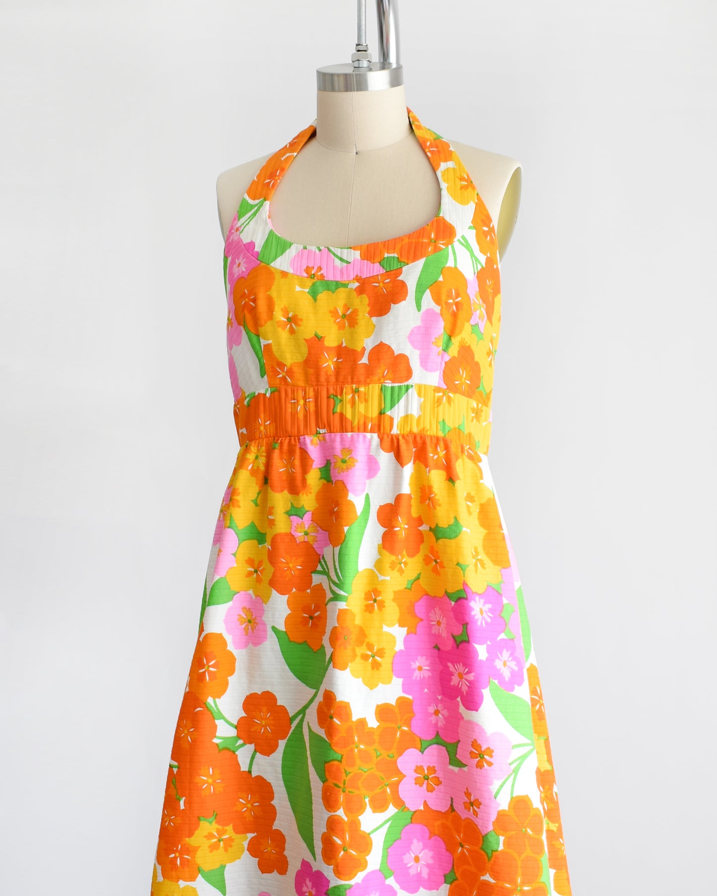 side front view of a vintage 1970s Hawaiian floral maxi dress by Malia. The dress is made from white ribbed cotton and has a large pink, yellow, orange, and green floral print covering the dress.