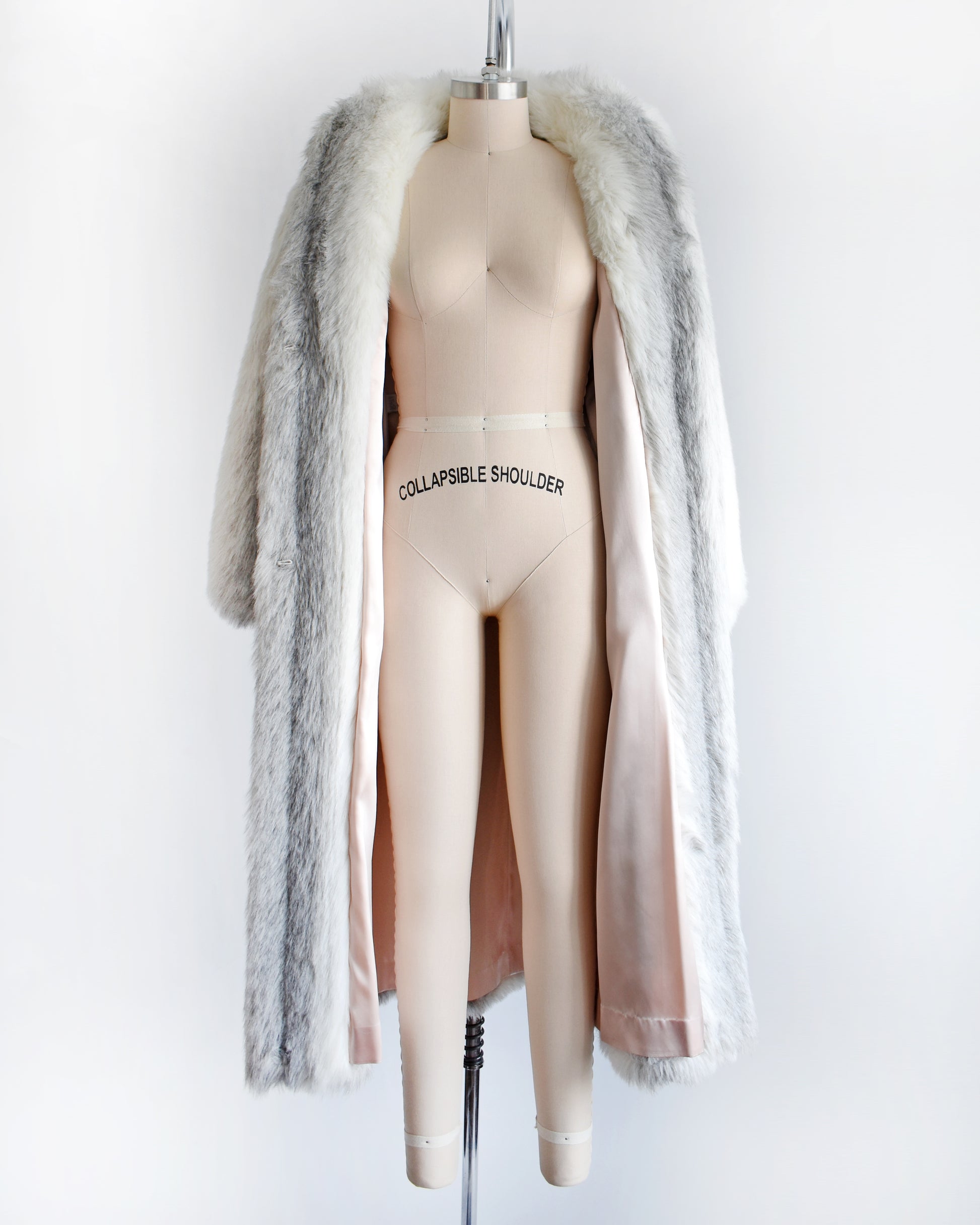 a vintage 1980s faux fur coat that's opening showing the light pink lining on a mannequin against a white background