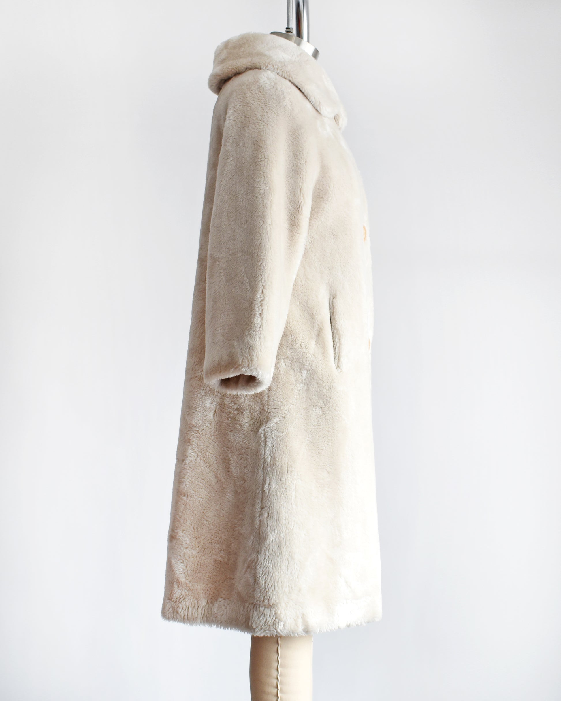 Side view of a vintage 1960s plush cream faux fur coat that features a Peter Pan style collar and three large buttons down the front