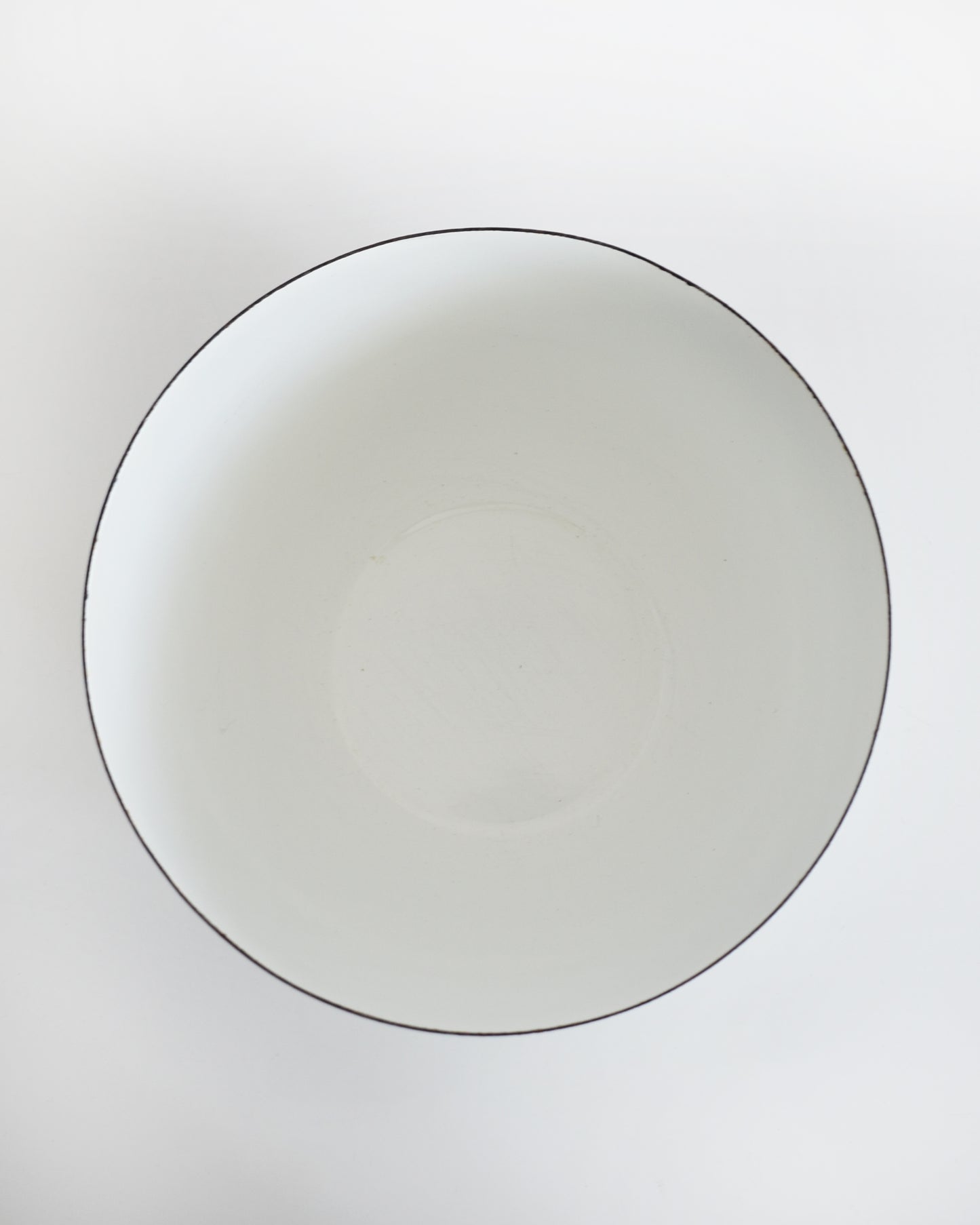 A top-down view of a white ceramic bowl with a thin black rim, set against a plain white background.