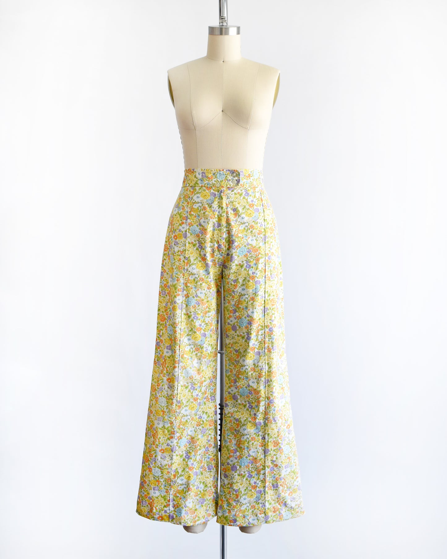 vintage 1970s yellow floral wide-leg pants displayed on a beige dress form mannequin against a white studio background.