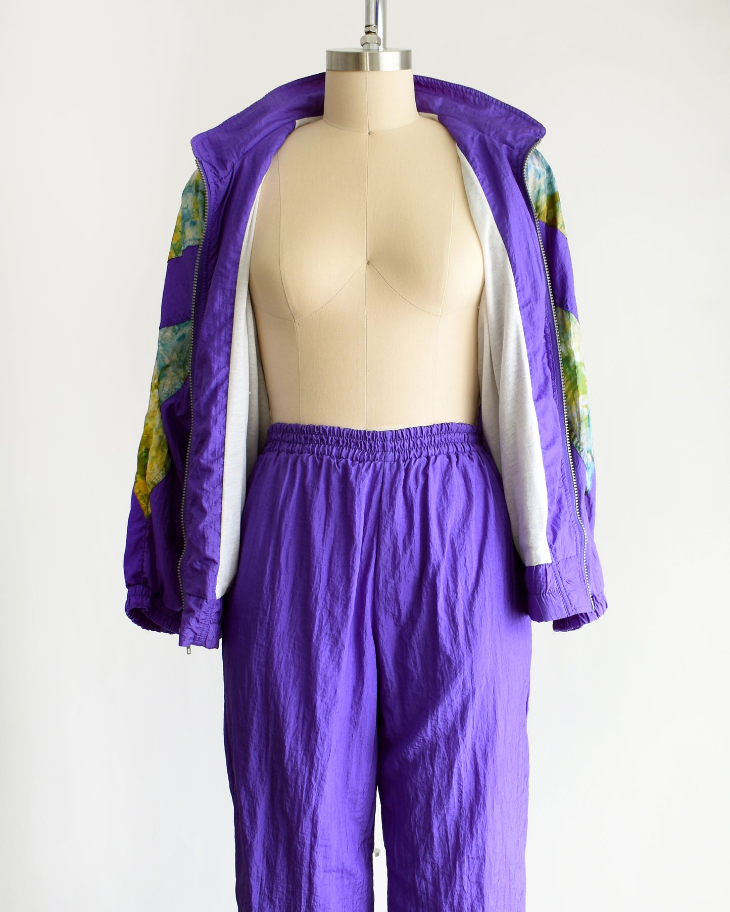 a vintage 1990s purple and multicolored tracksuit on a mannequin against a white background. the windbreaker is unzipped and open