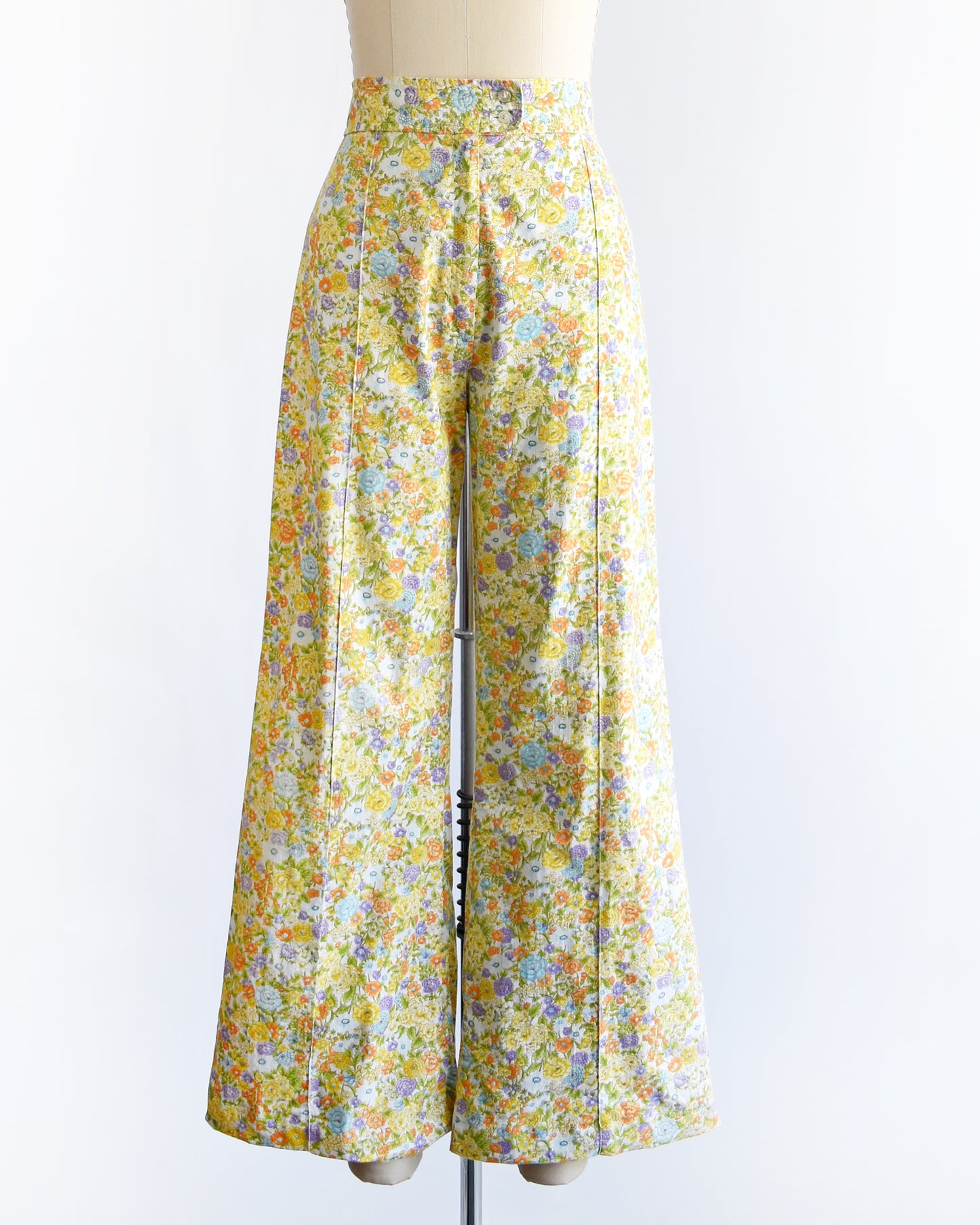 vintage 1970s yellow floral wide-leg pants displayed on a beige dress form mannequin against a white studio background.