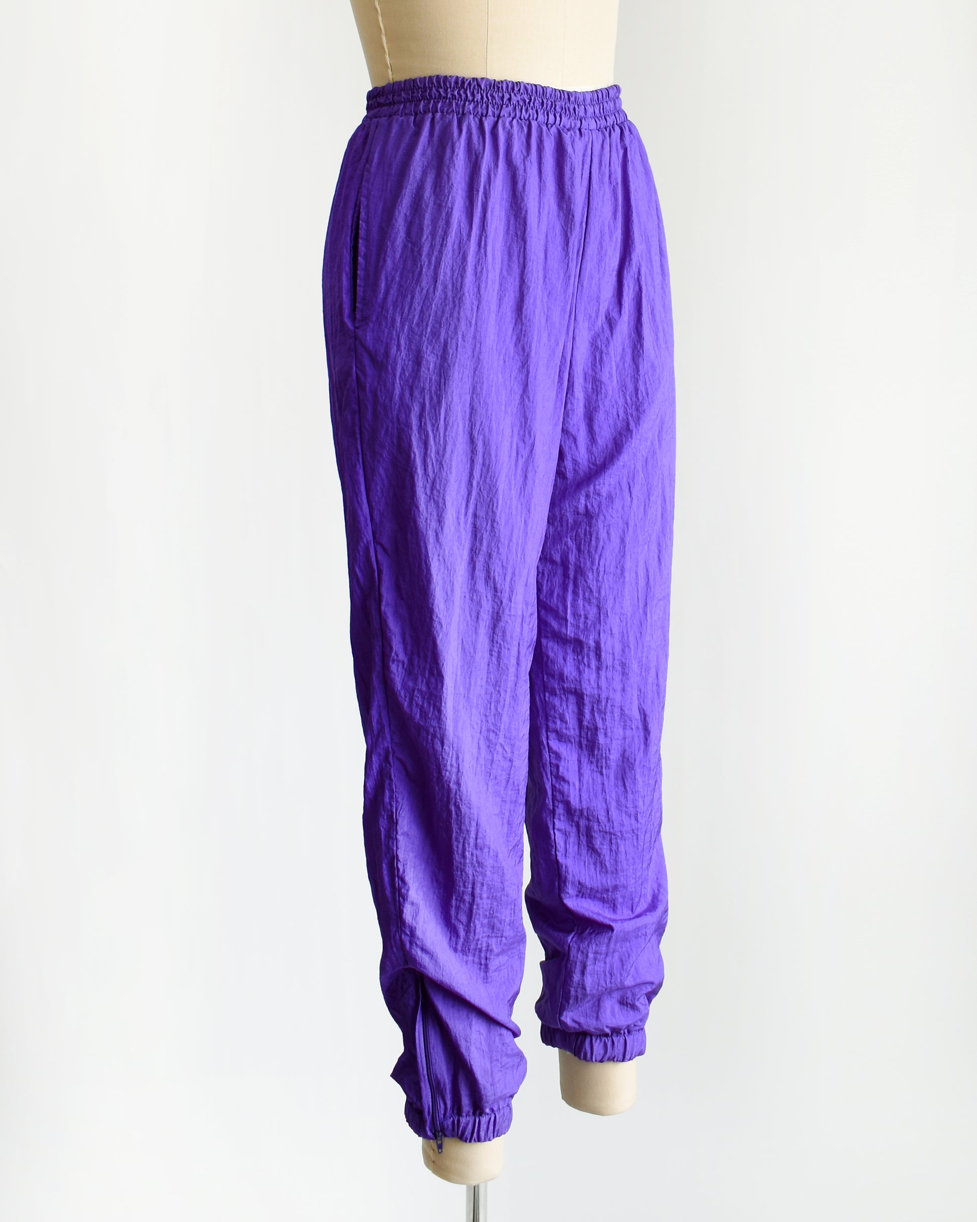 side font view of the pants from a  vintage 1990s purple  tracksuit on a mannequin against a white background