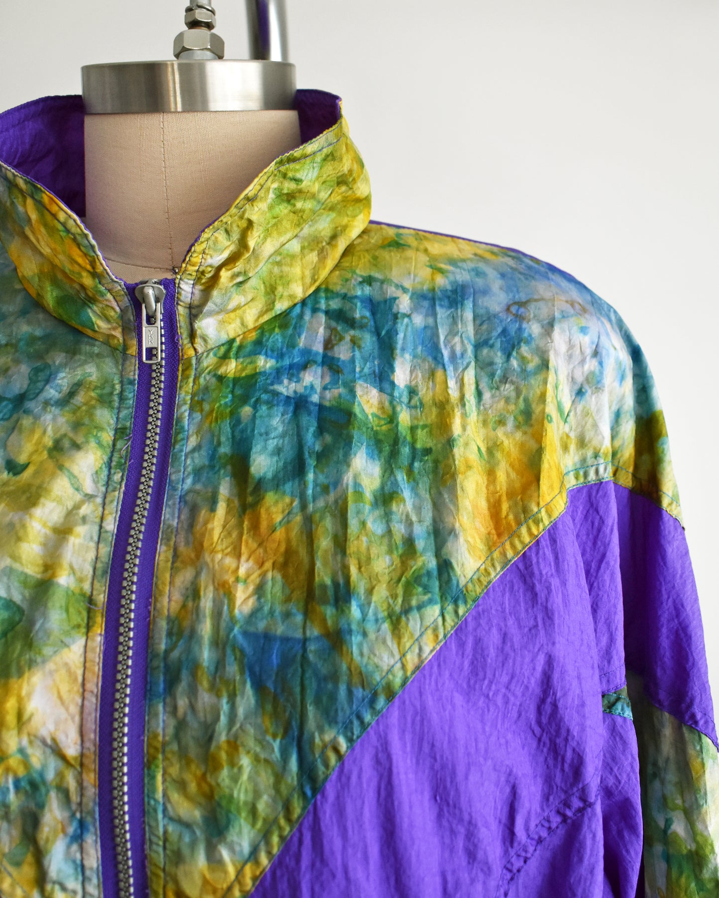 close up of the tie dyed print on a vintage 1990s purple and multicolored tracksuit on a mannequin against a white background