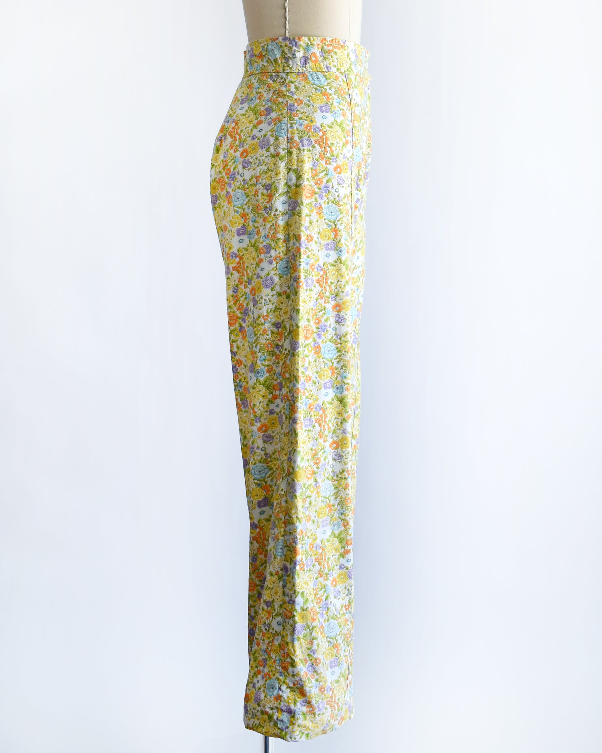 side view of vintage 1970s yellow floral wide-leg pants displayed on a beige dress form mannequin against a white studio background.