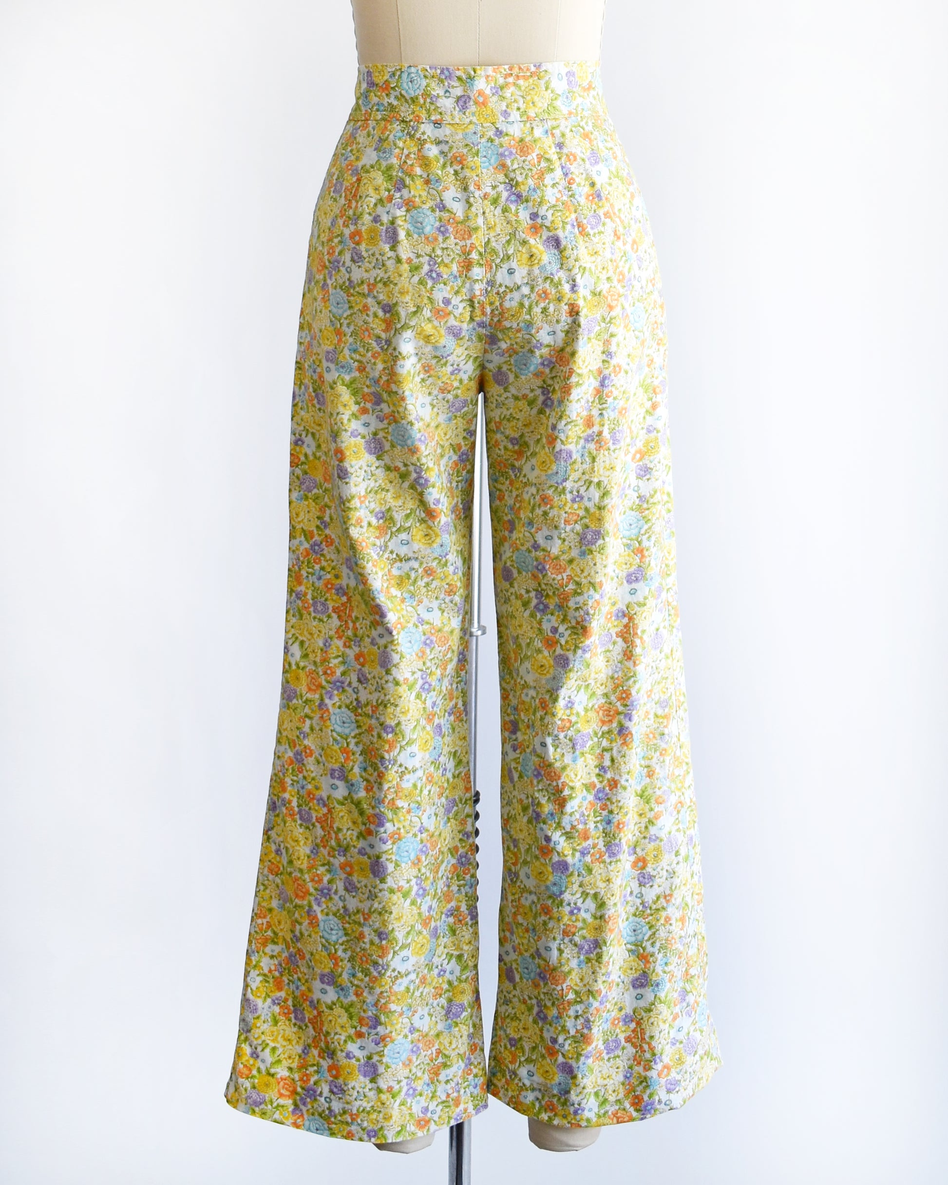 back view of vintage 1970s yellow floral wide-leg pants displayed on a beige dress form mannequin against a white studio background.