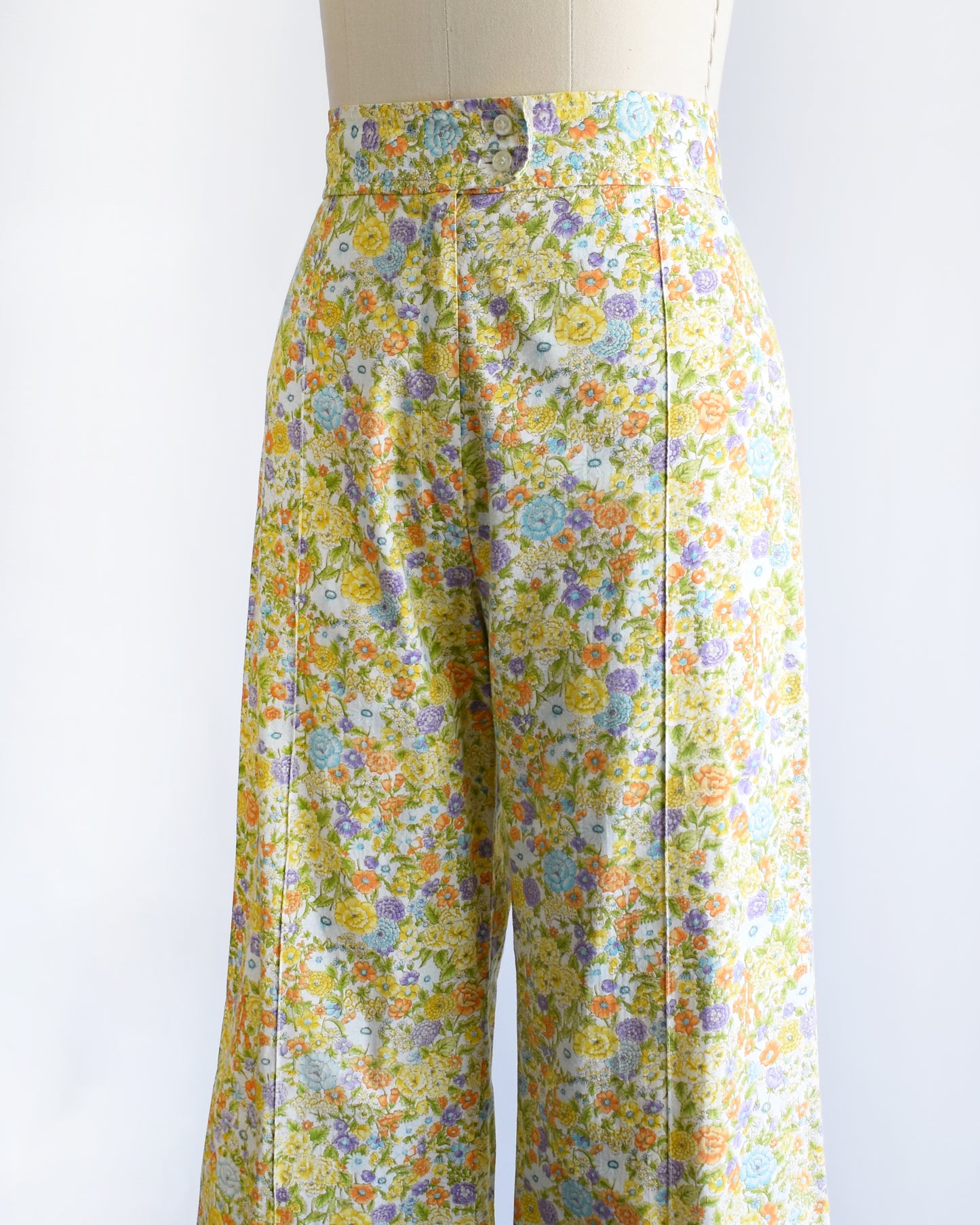 side front view of vintage 1970s yellow floral wide-leg pants displayed on a beige dress form mannequin against a white studio background.