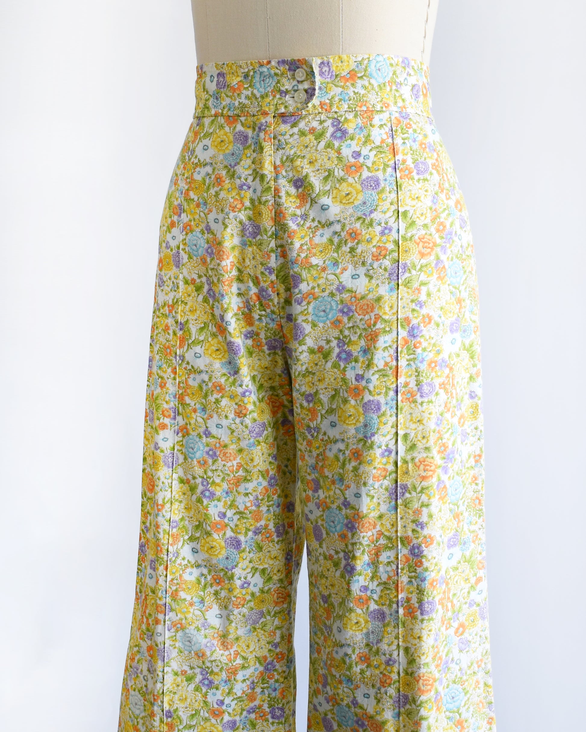 side front view of vintage 1970s yellow floral wide-leg pants displayed on a beige dress form mannequin against a white studio background.