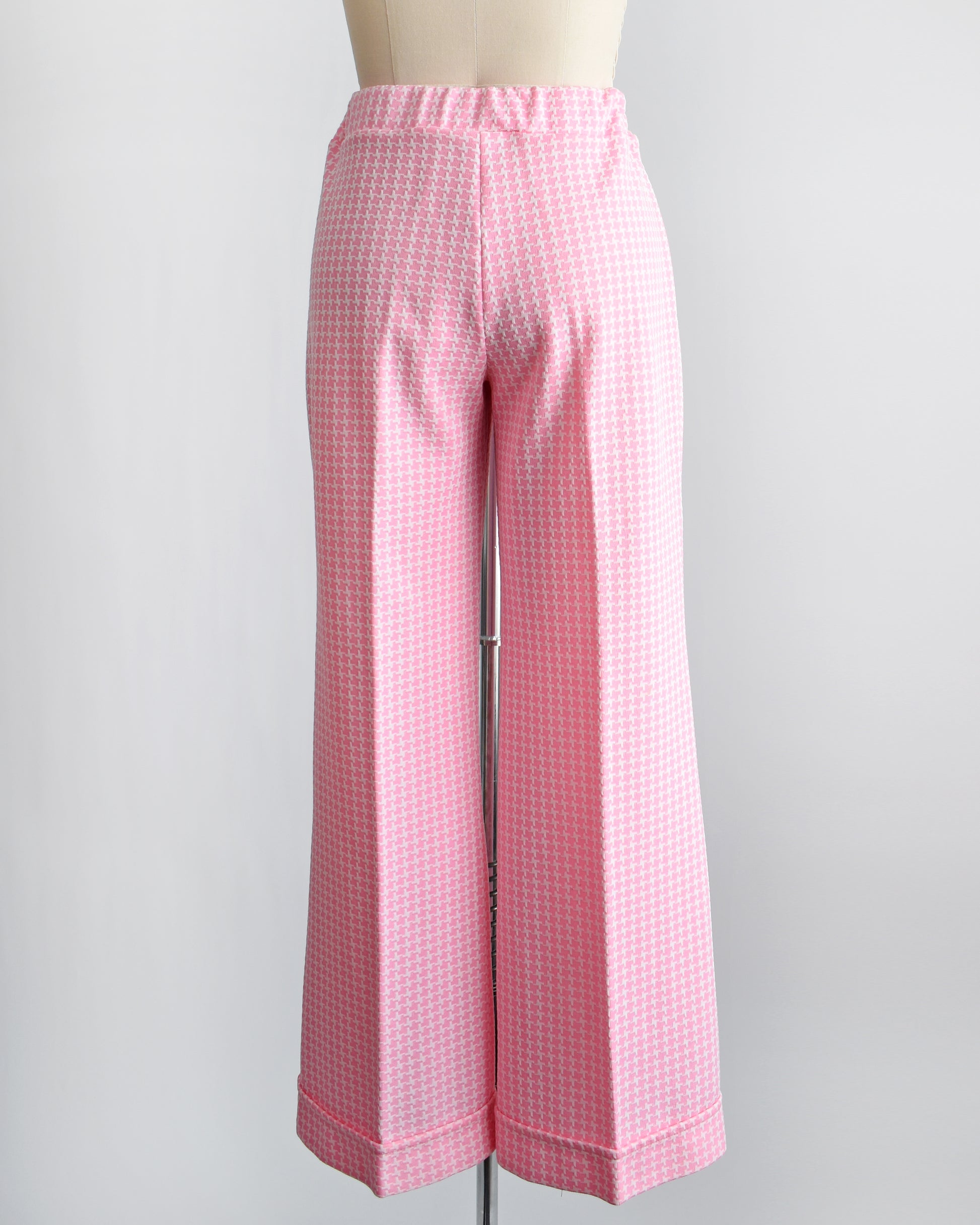 Back view of a vintage 1970s pink  and white houndstooth print wide leg pants on a dress form