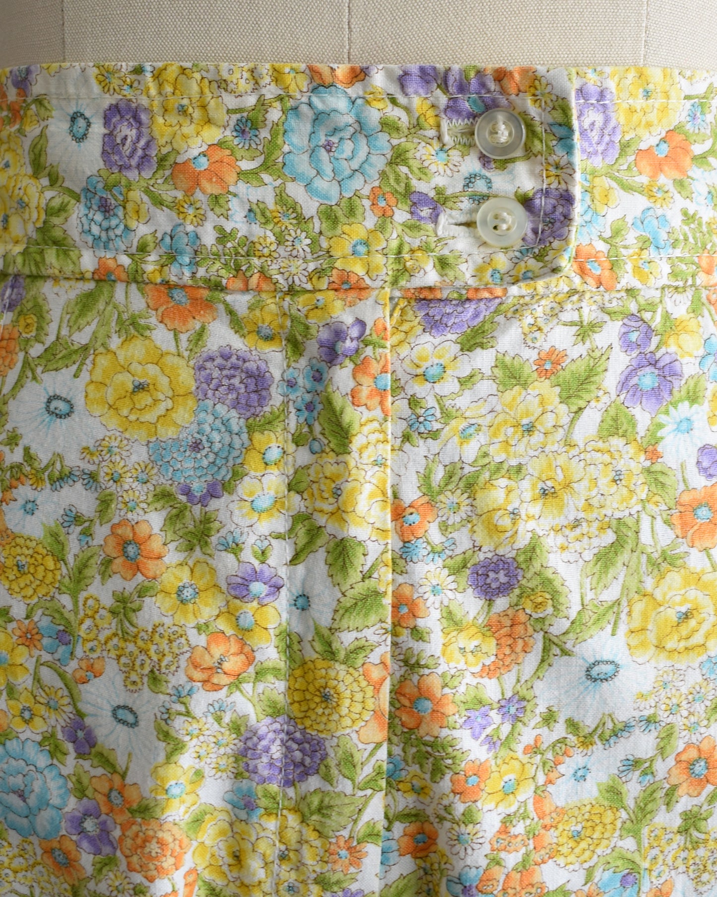 close up of the waist of vintage 1970s yellow floral wide-leg pants displayed on a beige dress form mannequin against a white studio background.