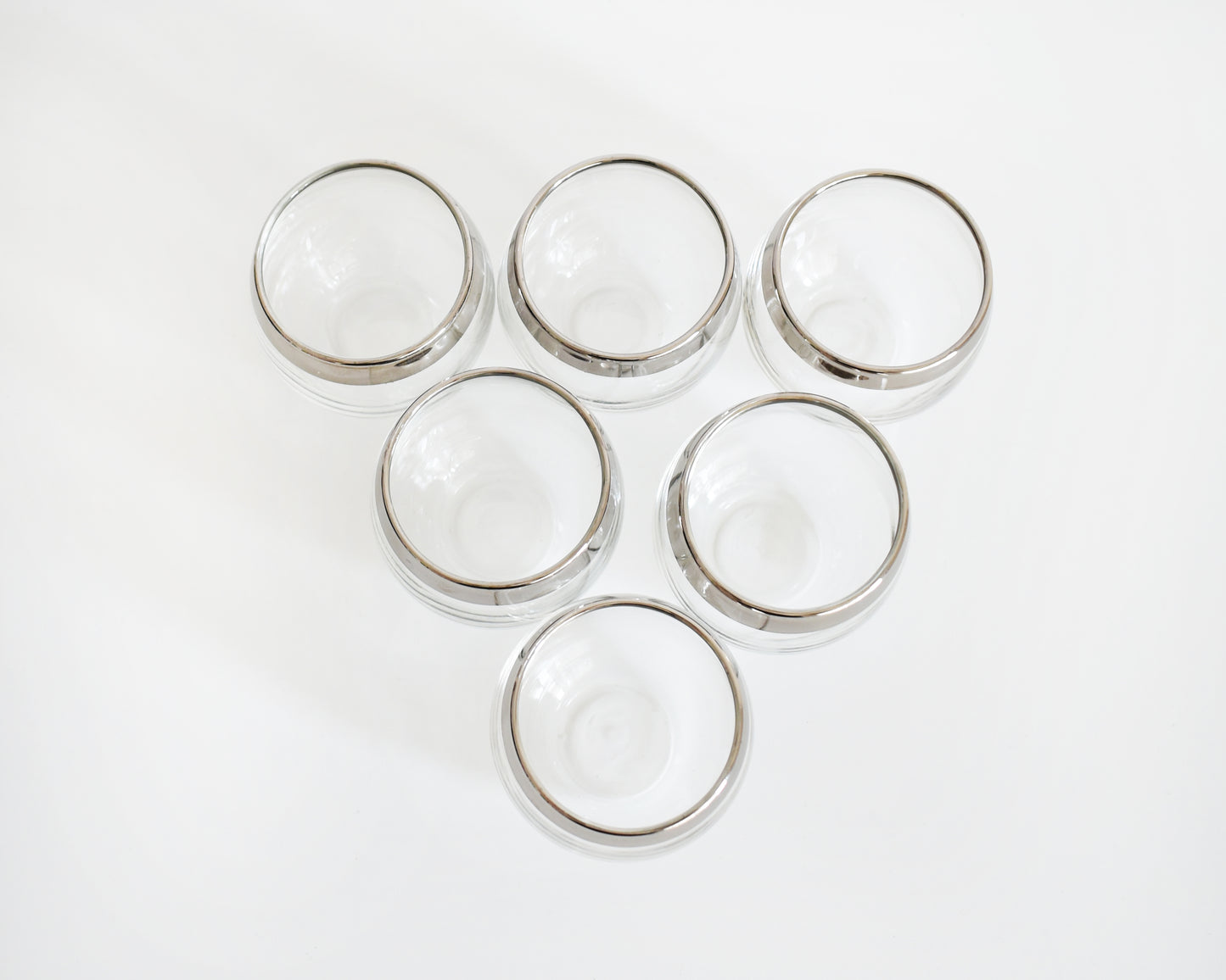 overhead shot of six clear roly poly glasses with polished silver rims, arranged in rows on a plain white background.