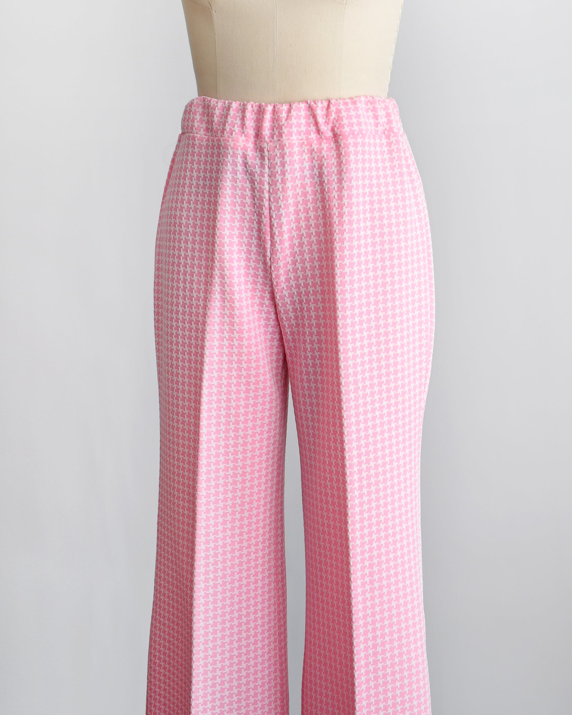 Side front view of the waist of vintage 1970s pink  and white houndstooth print wide leg pants on a dress form