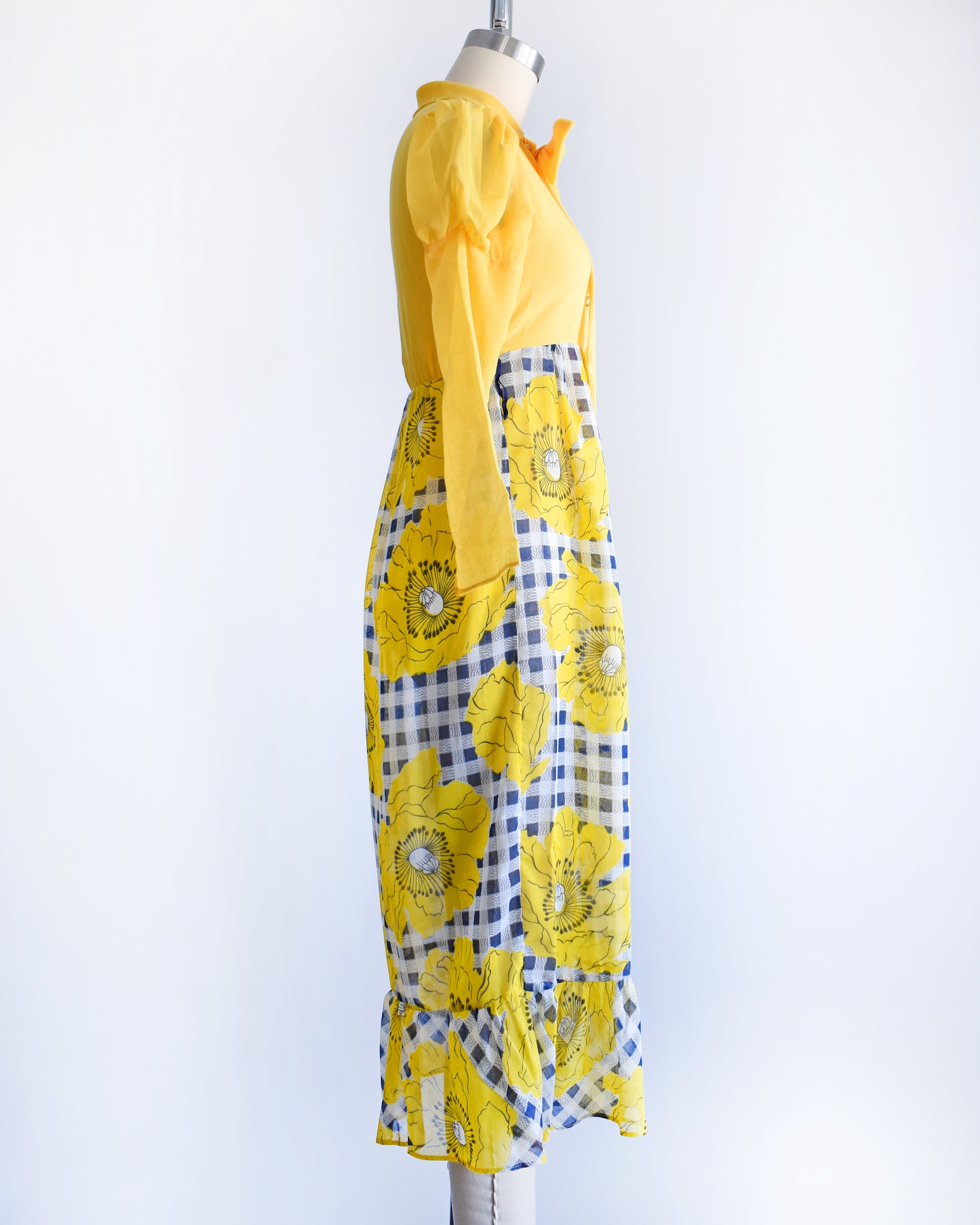 side view of a vintage 1960s 1970s yellow and black floral dress on a mannequin against a white background