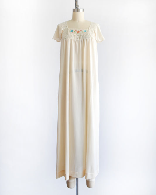 a vintage 1970s cream-colored nightgown with short sleeves and delicate floral embroidery across the chest, displayed on a dress form mannequin against a white background.