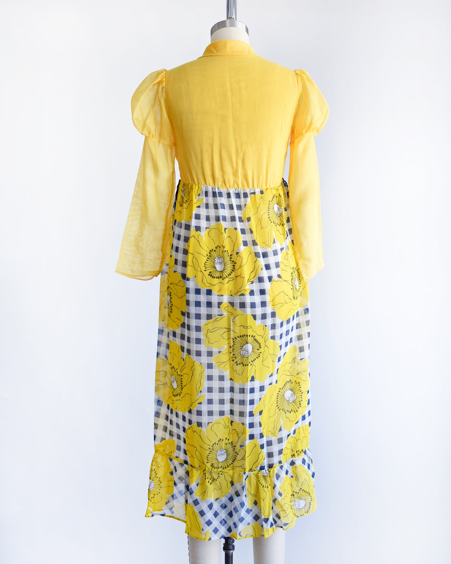 back view of a vintage 1960s 1970s yellow and black floral dress on a mannequin against a white background