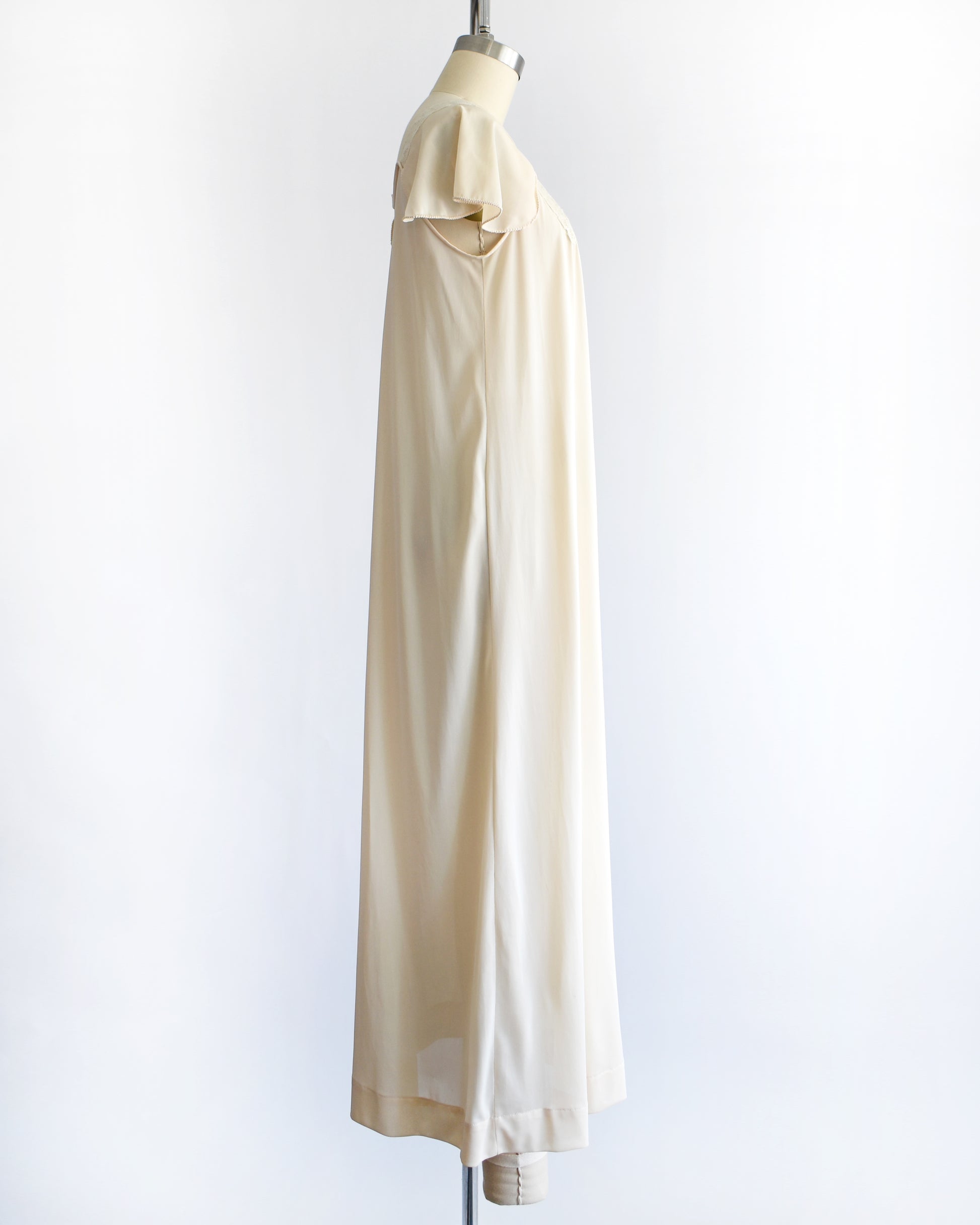 side view of a vintage 1970s cream-colored nightgown with short sleeves and delicate floral embroidery across the chest, displayed on a dress form mannequin against a white background.