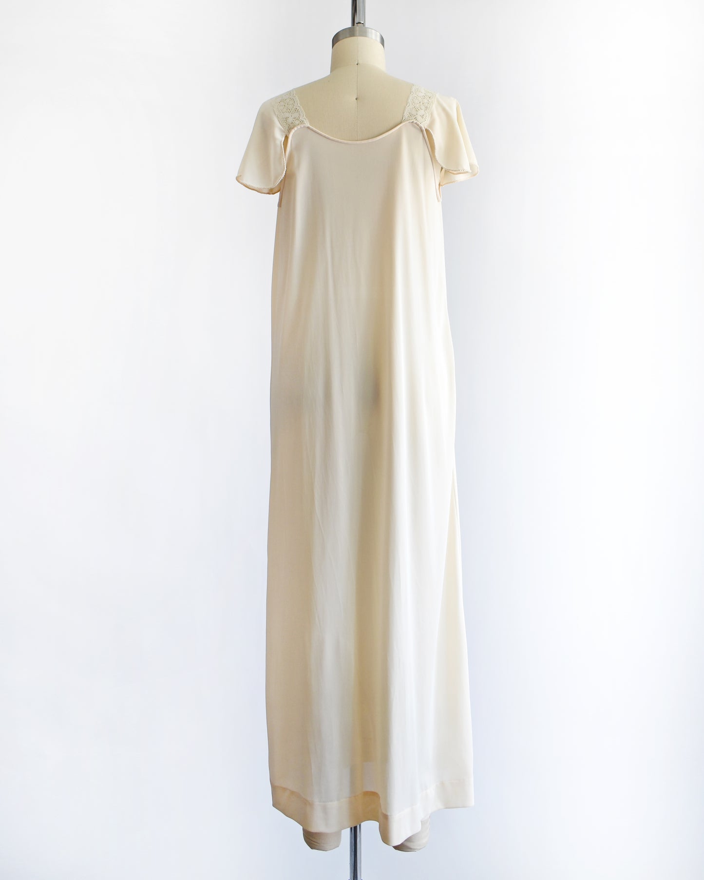 back view of a vintage 1970s cream-colored satin nightgown with short flutter sleeves and a scoop neckline, displayed on a dress form mannequin against a plain white background