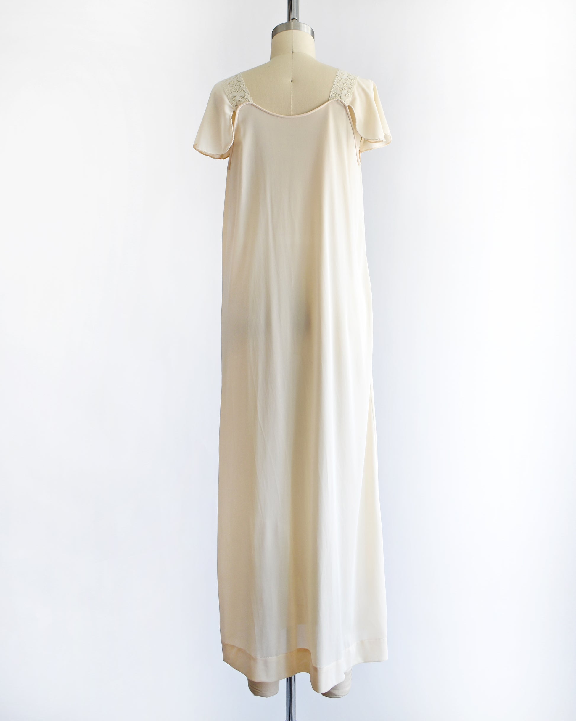 back view of a vintage 1970s cream-colored satin nightgown with short flutter sleeves and a scoop neckline, displayed on a dress form mannequin against a plain white background