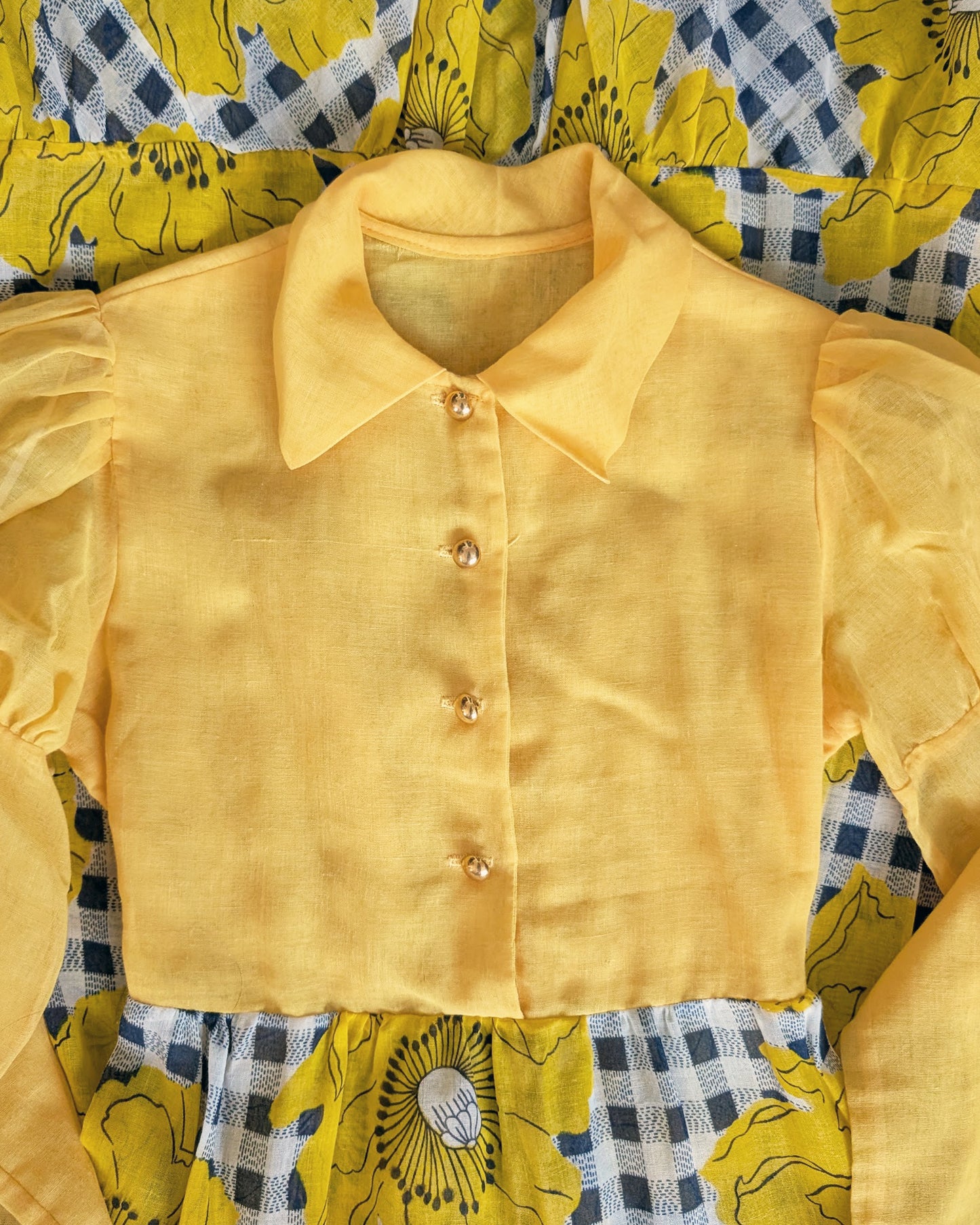 flat lay of a vintage 1960s 1970s yellow and black floral dress with out it's bow on a mannequin against a white background