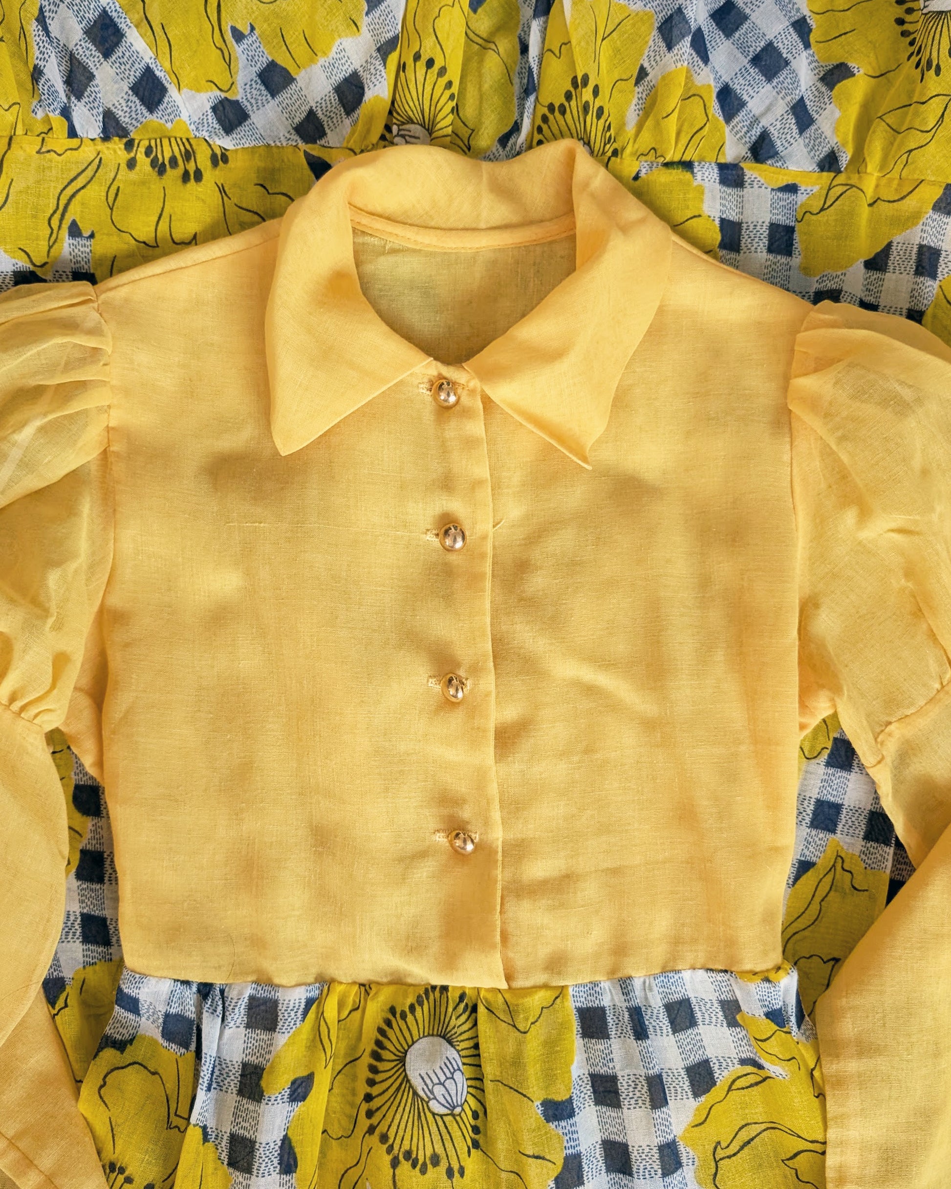 flat lay of a vintage 1960s 1970s yellow and black floral dress with out it's bow on a mannequin against a white background
