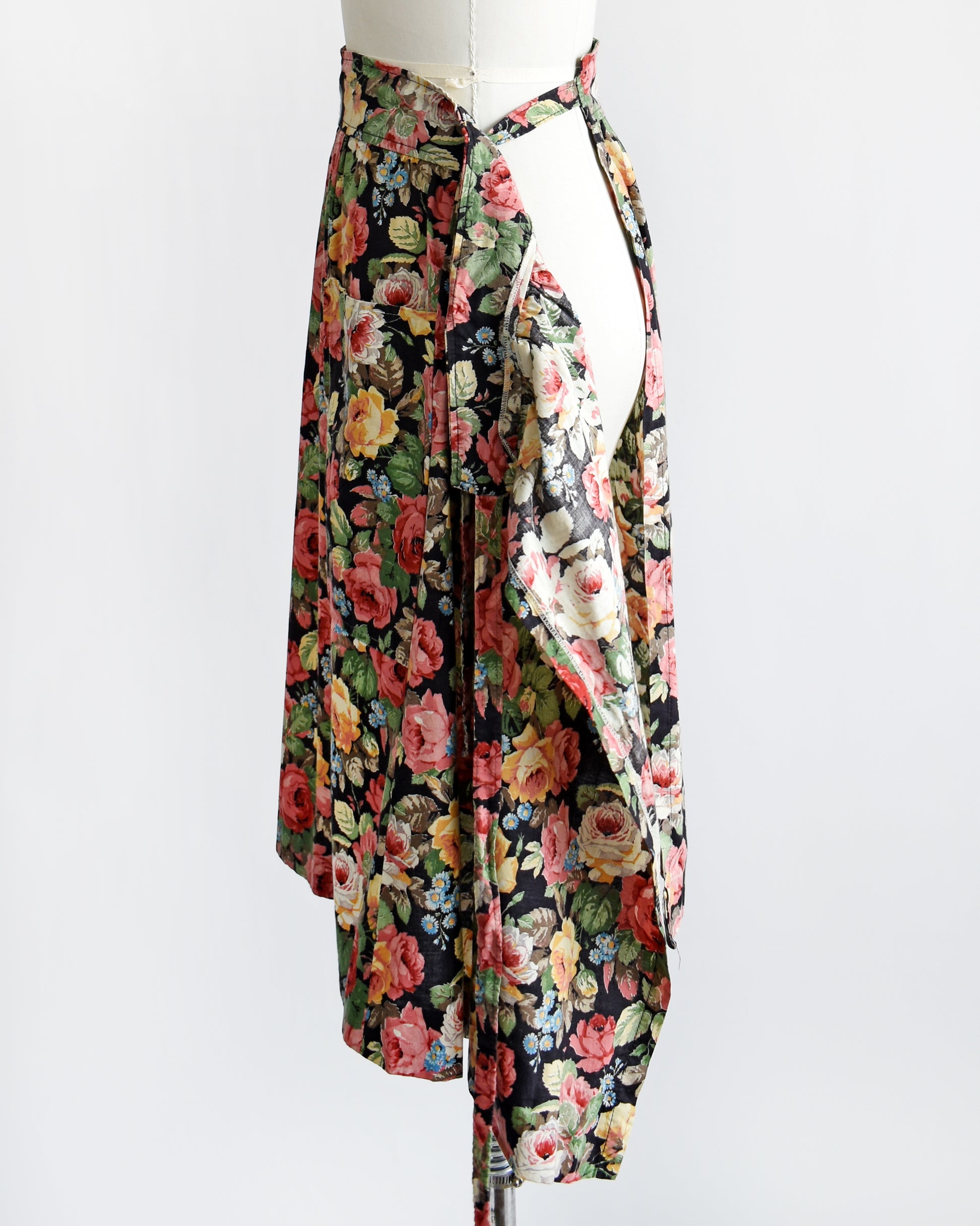 side view of a vintage 1970s black floral wrap skirt that has two large pockets on the front. the skirt is untied in this photo showing the wrap of the waistband