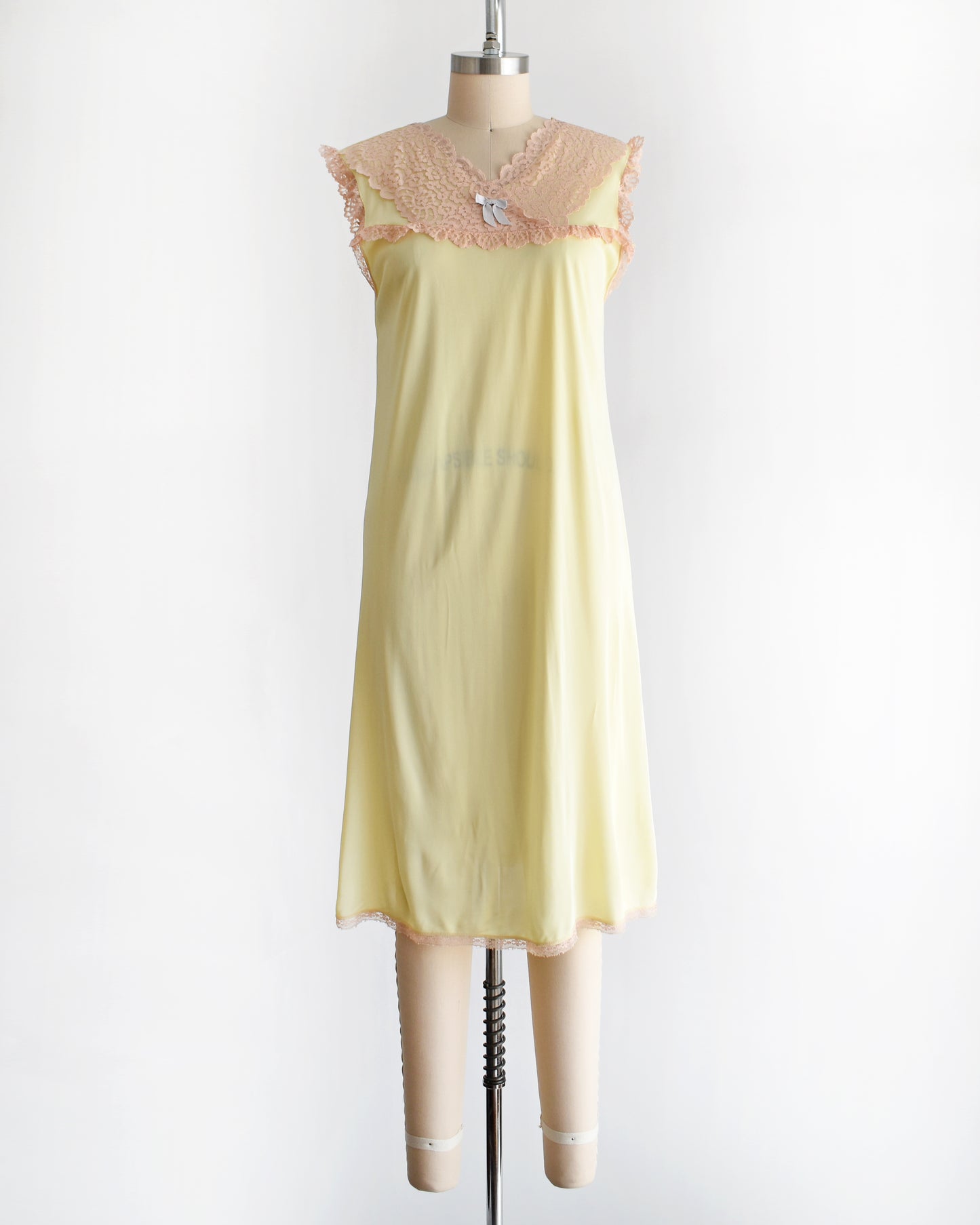 A vintage 1960s pale yellow slip-style nightgown with a peach lace yoke and ruffled trim, displayed on a mannequin against a plain white background.
