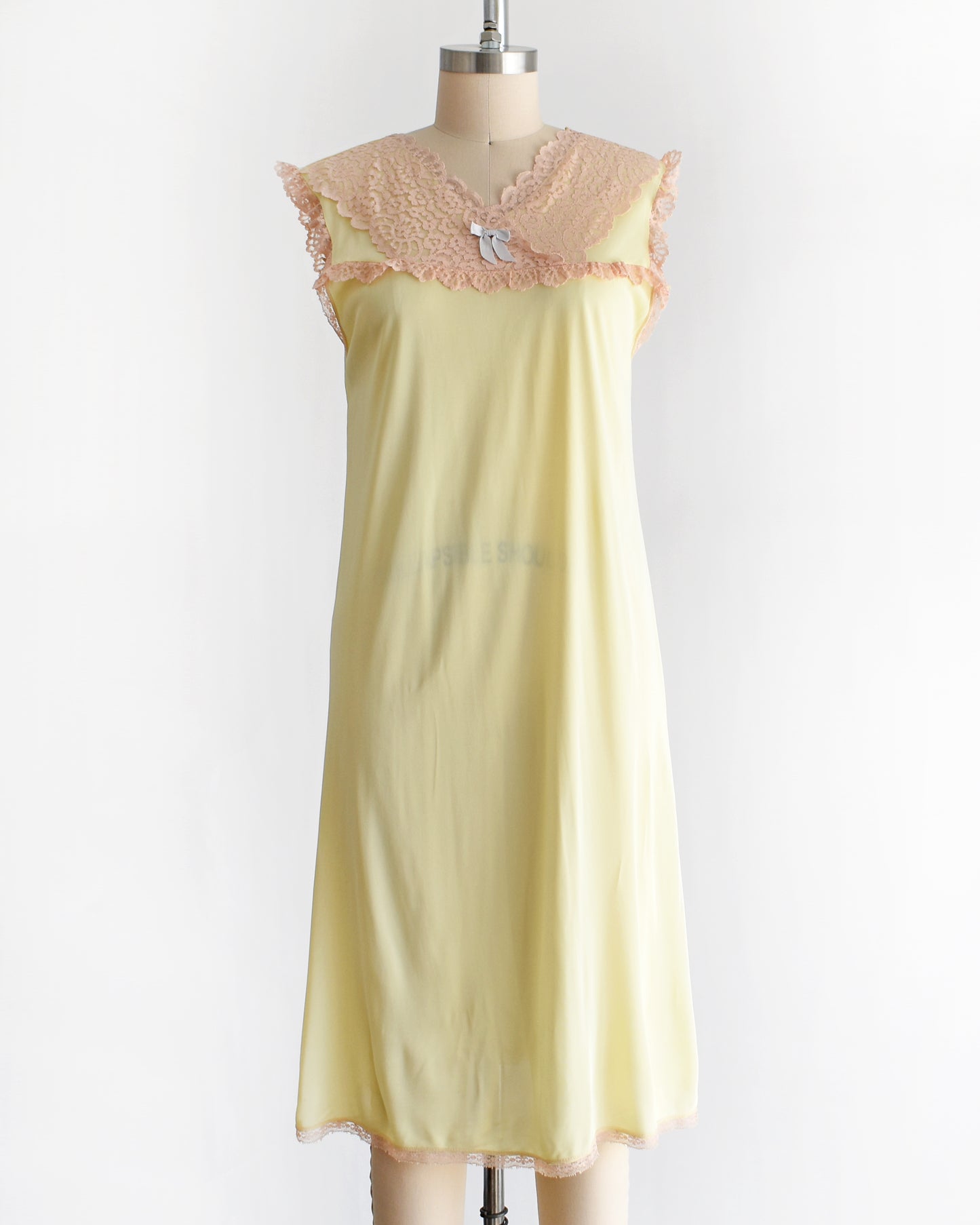 A vintage 1960s pale yellow slip-style nightgown with a peach lace yoke and ruffled trim, displayed on a mannequin against a plain white background.