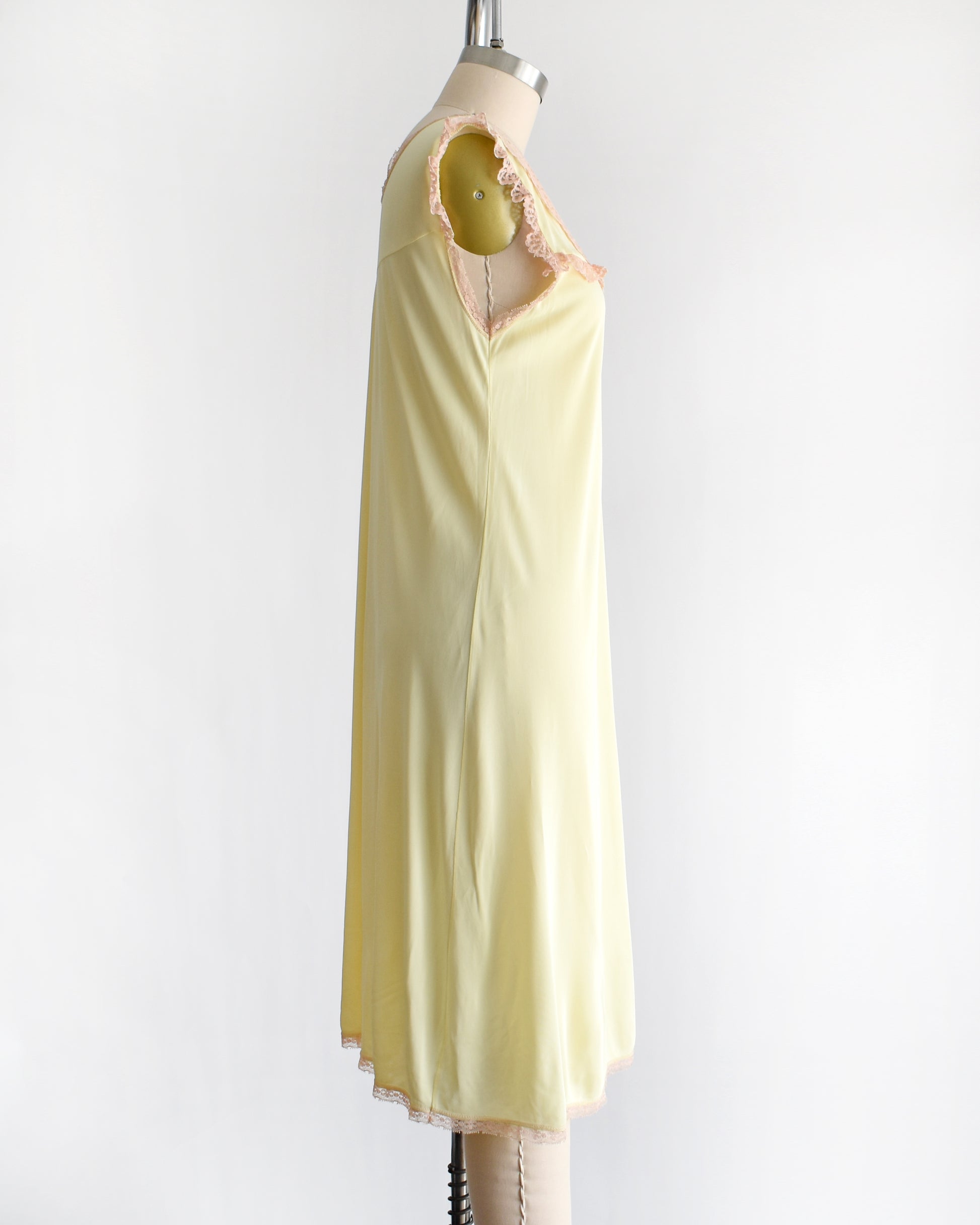 side view of a vintage 1960s pale yellow slip-style nightgown with a peach lace yoke and ruffled trim, displayed on a mannequin against a plain white background.