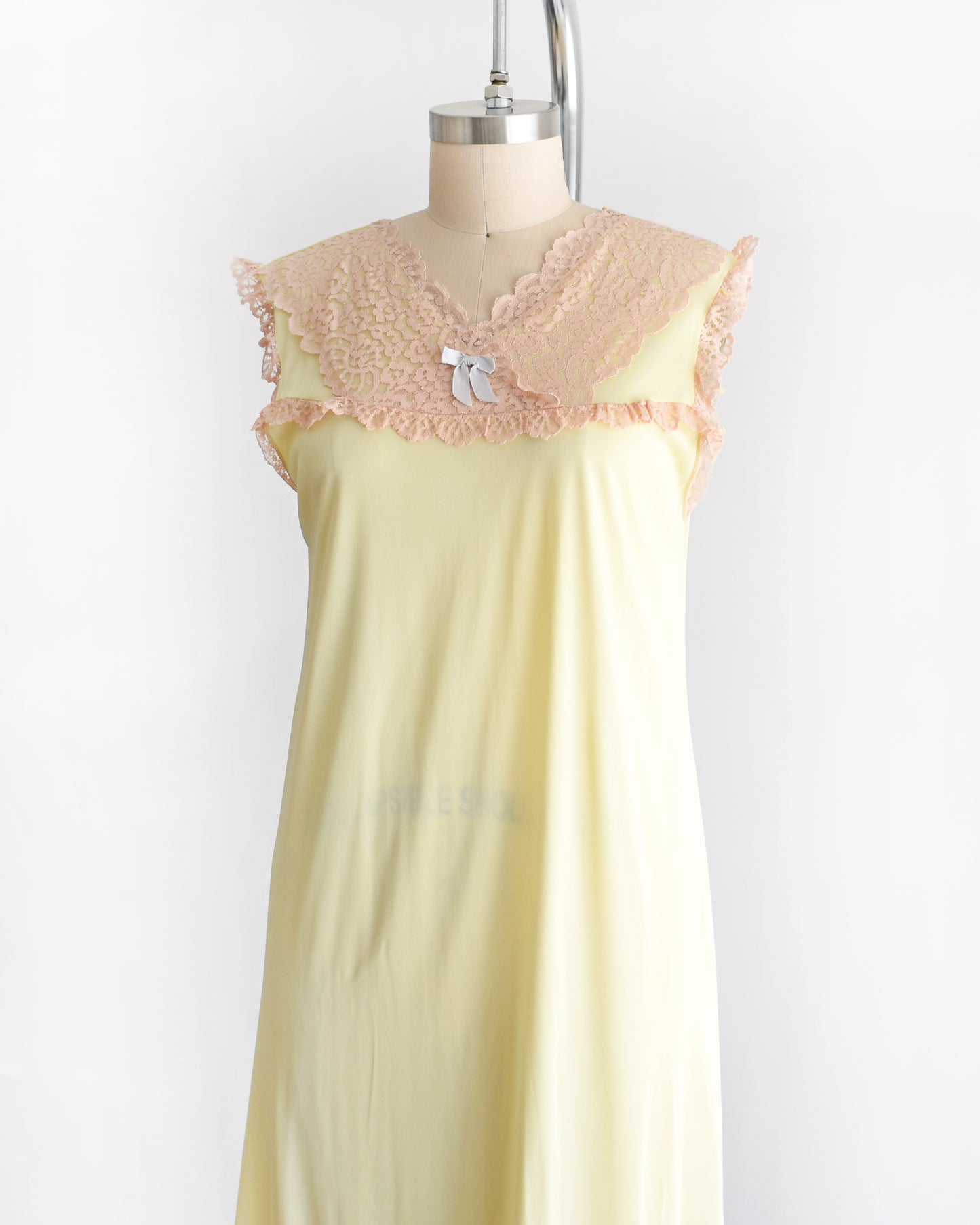 side front view of a vintage 1960s pale yellow slip-style nightgown with a peach lace yoke and ruffled trim, displayed on a mannequin against a plain white background.