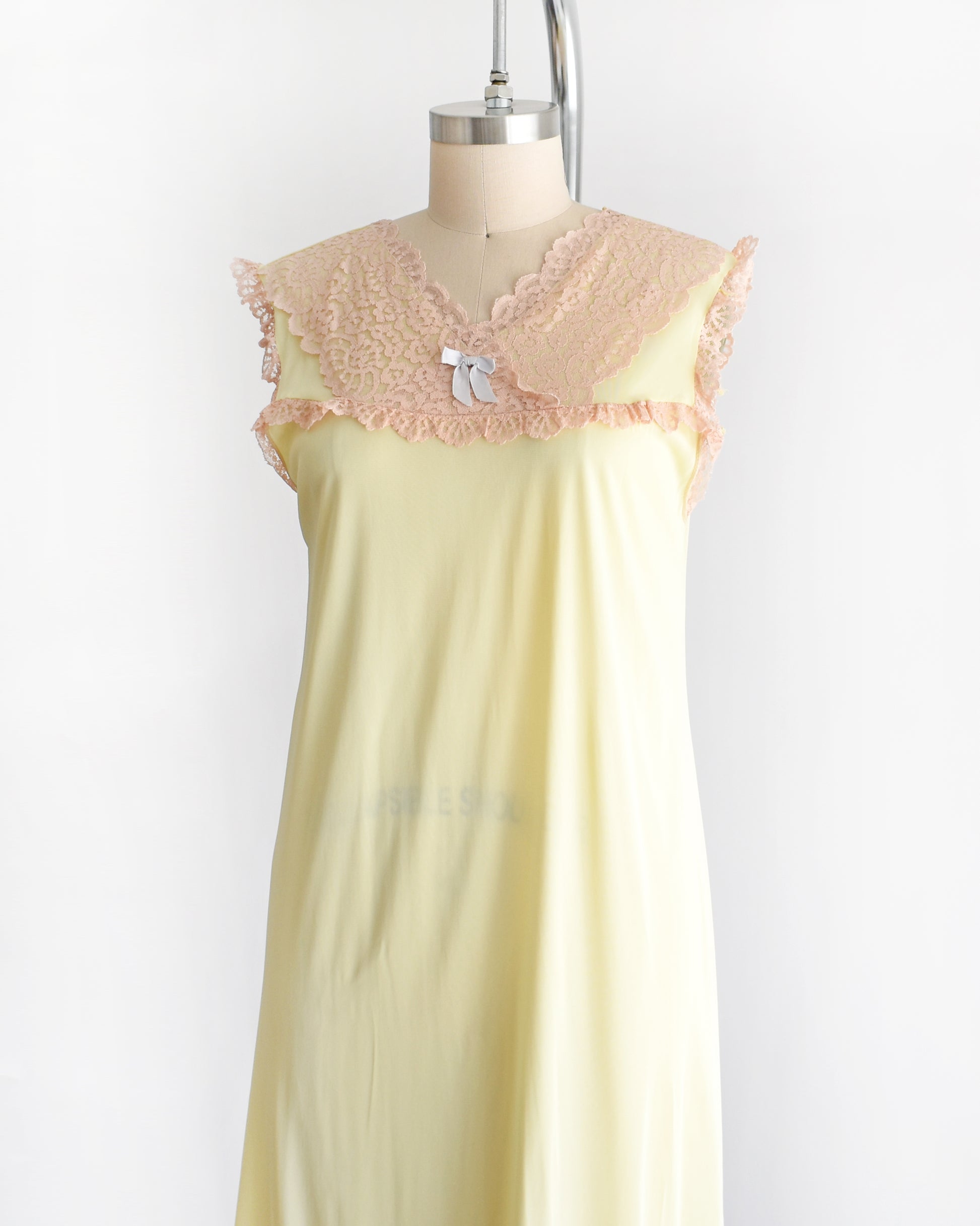 side front view of a vintage 1960s pale yellow slip-style nightgown with a peach lace yoke and ruffled trim, displayed on a mannequin against a plain white background.