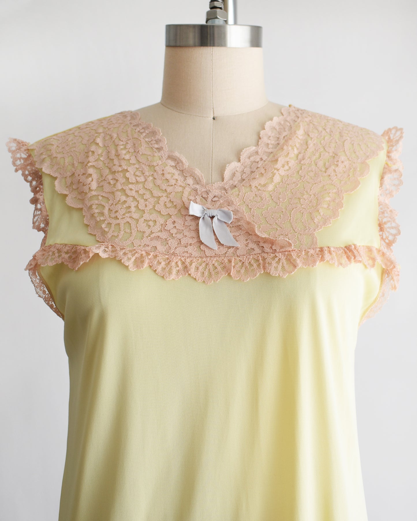 close up of the bodice on a vintage 1960s pale yellow slip-style nightgown with a peach lace yoke and ruffled trim, displayed on a mannequin against a plain white background.