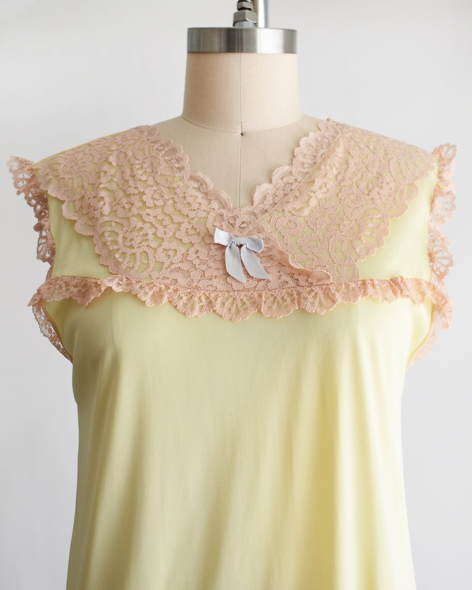 close up of the bodice on a vintage 1960s pale yellow slip-style nightgown with a peach lace yoke and ruffled trim, displayed on a mannequin against a plain white background.