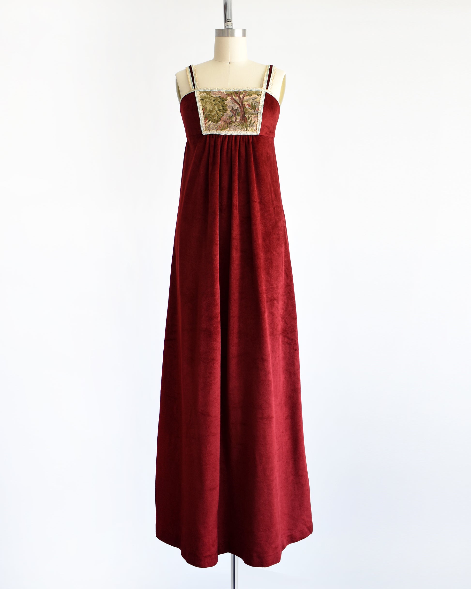 A vintage 1970s burgundy velvet maxi dress that has a woodsy tapestry scene on the bodice.