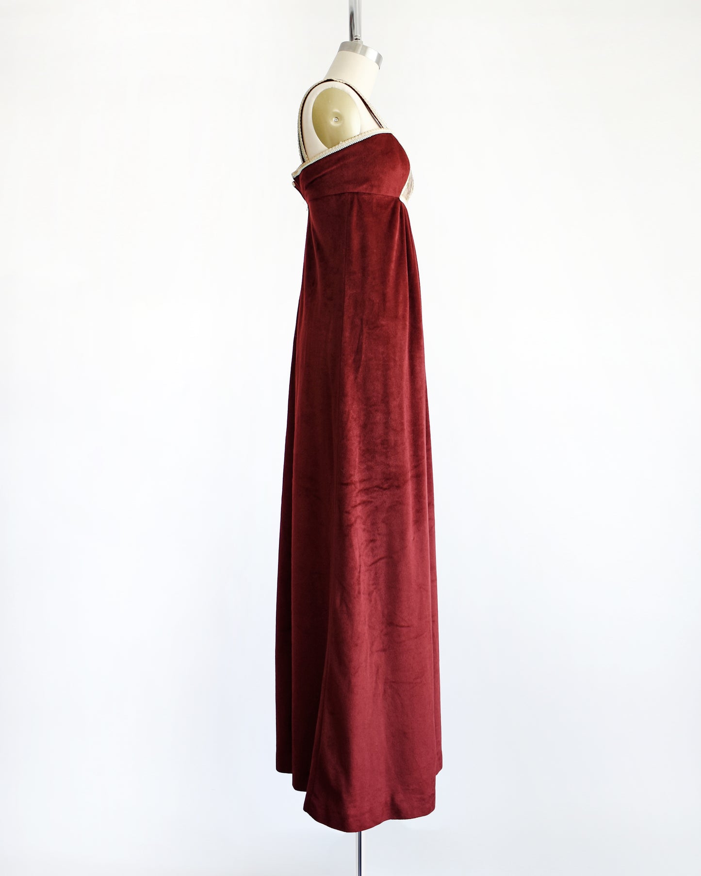 side view of A vintage 1970s burgundy velvet maxi dress that has a woodsy tapestry scene on the bodice.