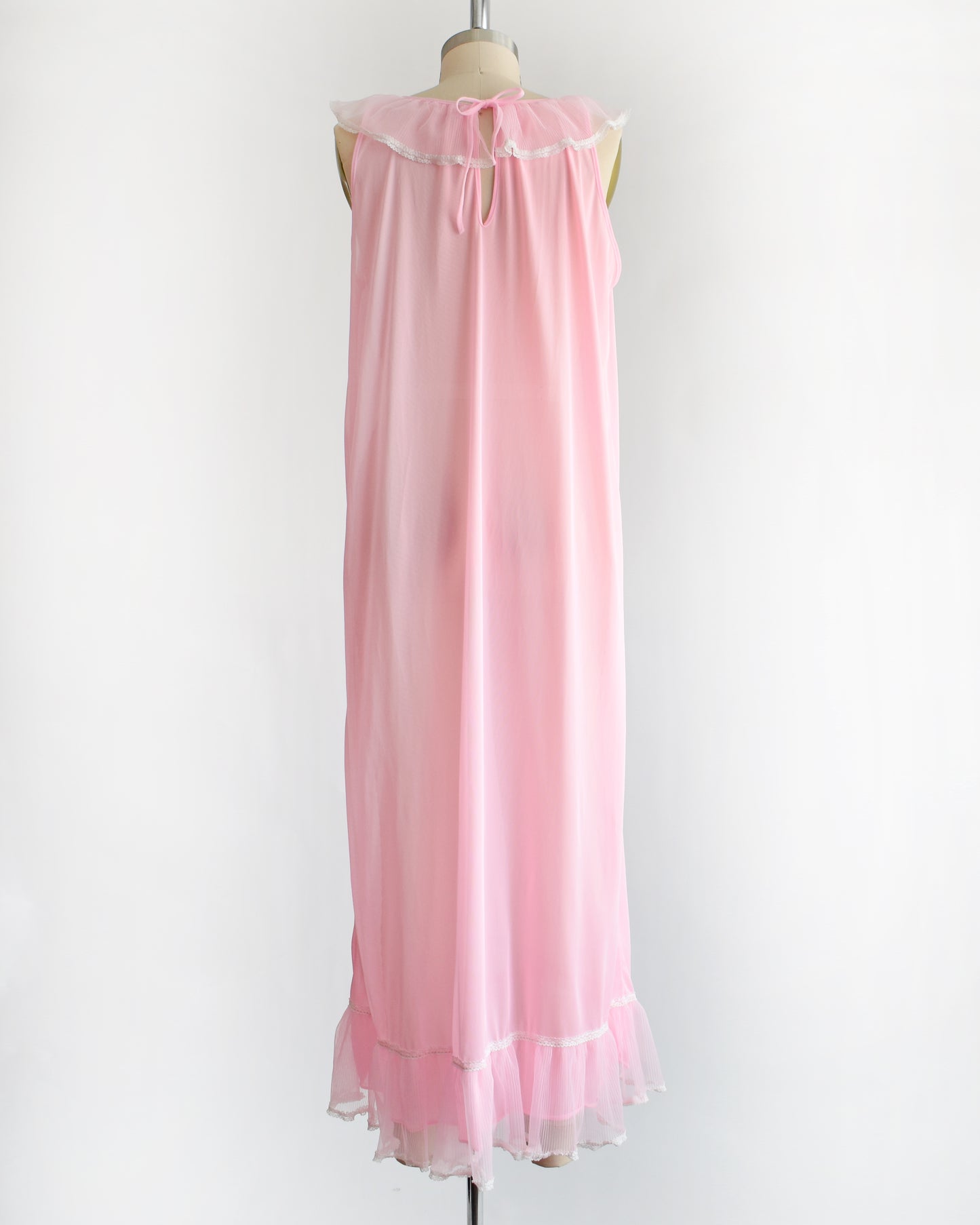 back view of a vintage 1970s sleeveless pink nightgown with a ruffled collar and hem, displayed on a dress form against a plain white background.