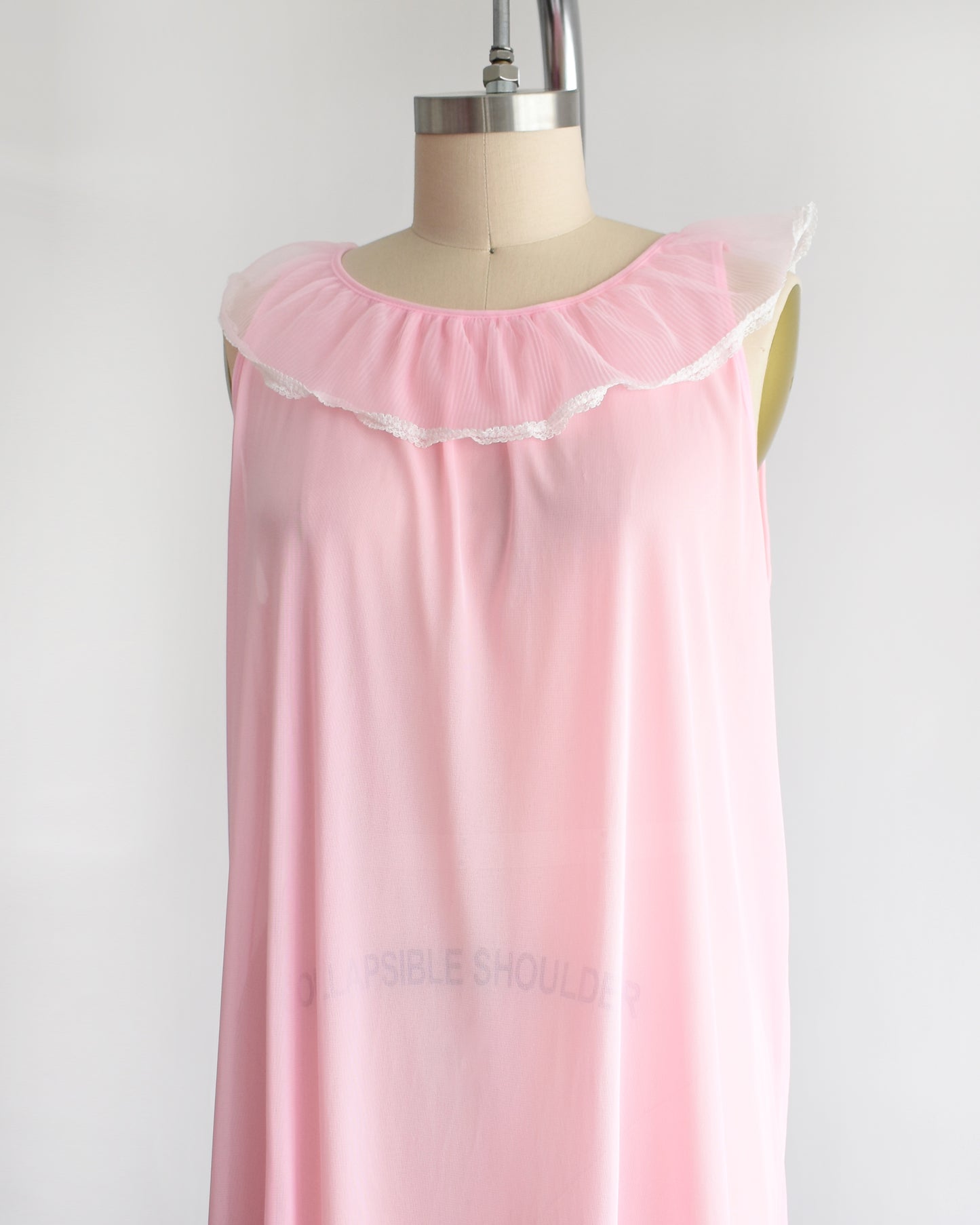 side front view of a vintage 1970s sleeveless pink nightgown with a ruffled collar and hem, displayed on a dress form against a plain white background.