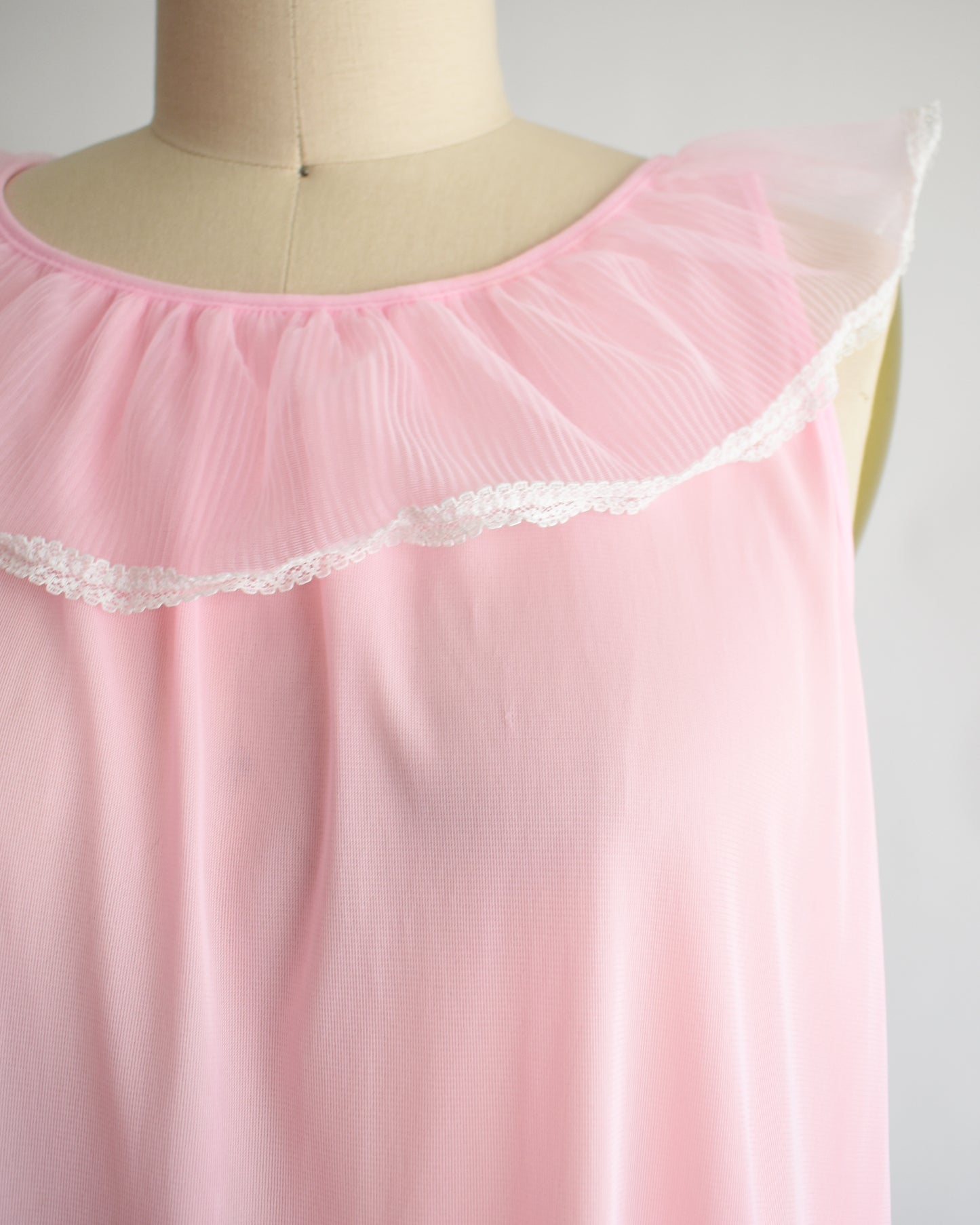 close up of the bodice on a vintage 1970s sleeveless pink nightgown with a ruffled collar and hem, displayed on a dress form against a plain white background.