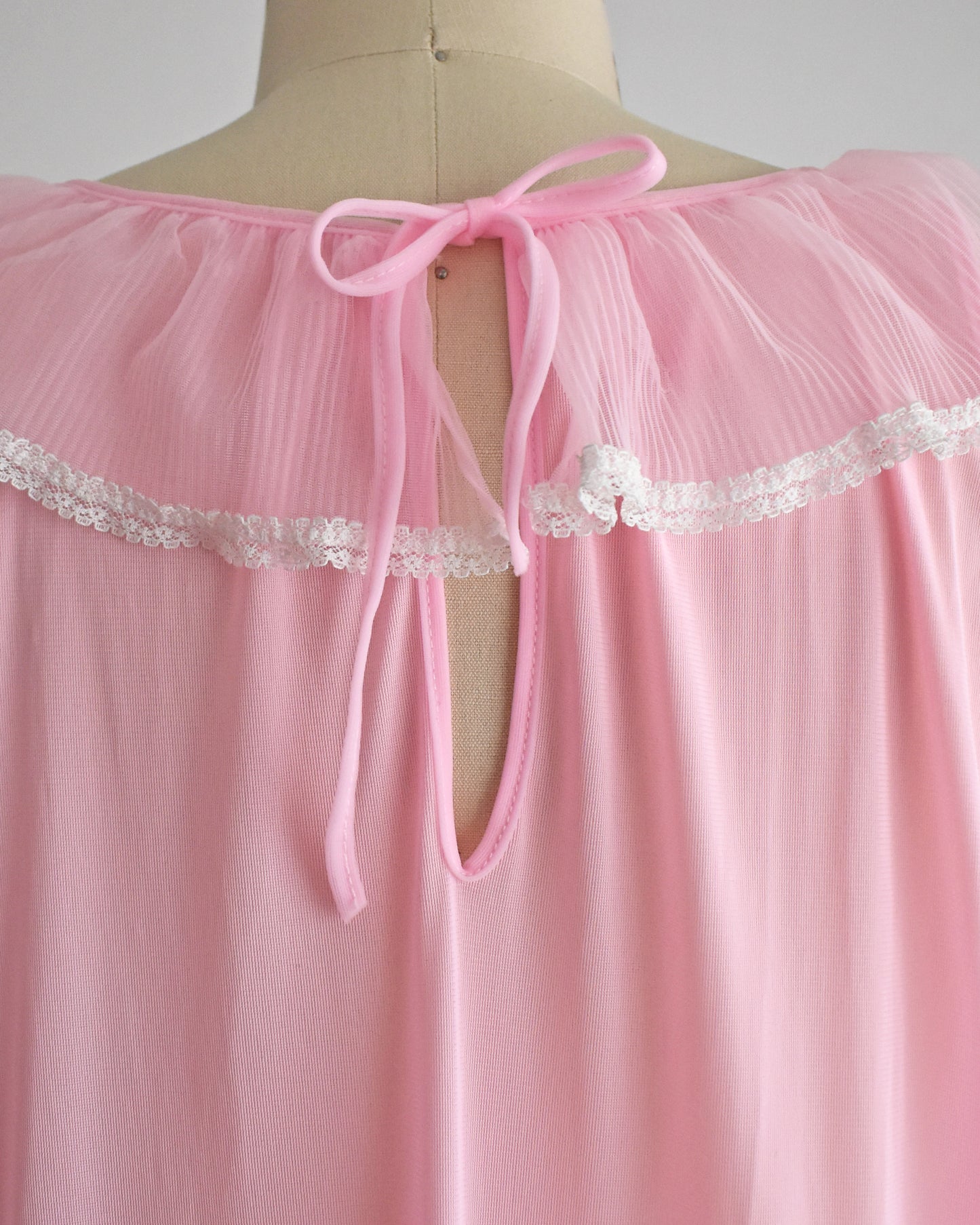 back view of the pink nightgown with a tie-neck design and white lace trim, displayed on a mannequin torso.
